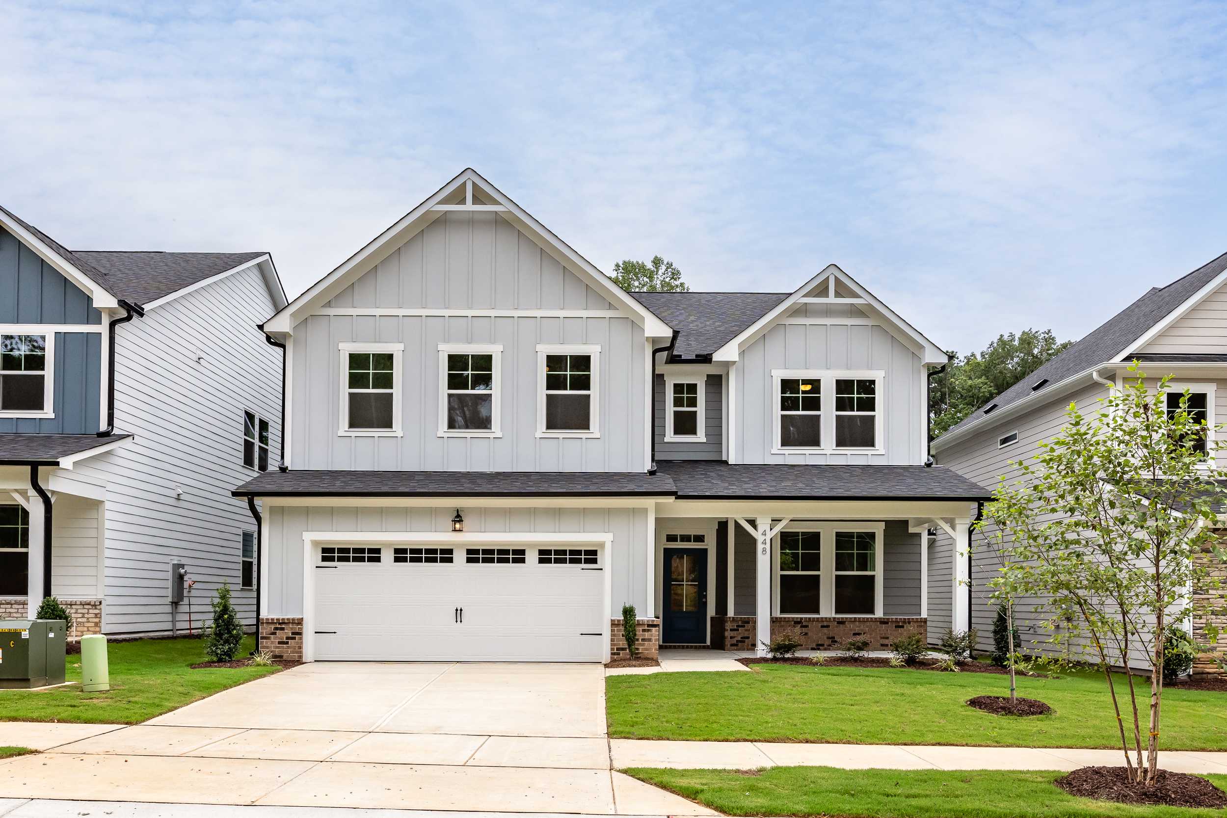 Modern farmhouse home exterior at Enclave at Belmont in NC with covered porch, two-car garage, and lush landscaping