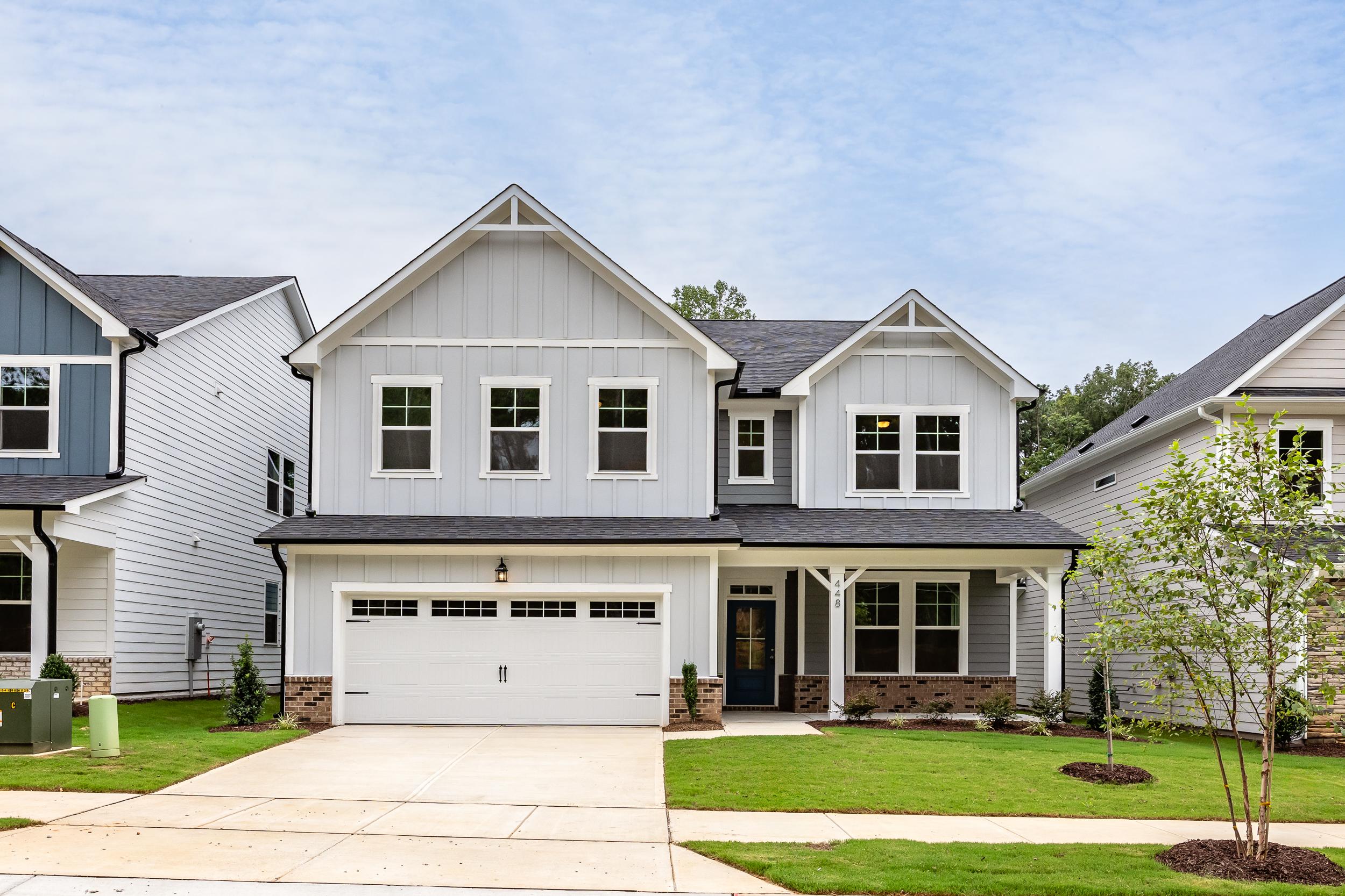 The Aspen B two-story home elevation with gray vinyl siding, brick accents, two-car garage, and front porch in Holly Springs NC