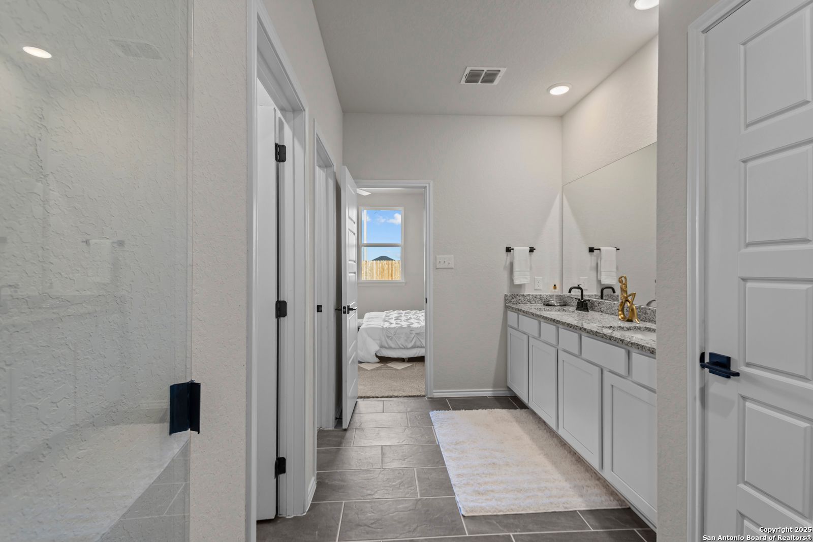 Modern master bathroom with dual vanities, gold faucets, glass shower, and bedroom view in Davidson Homes The Douglas C, Seguin, Texas