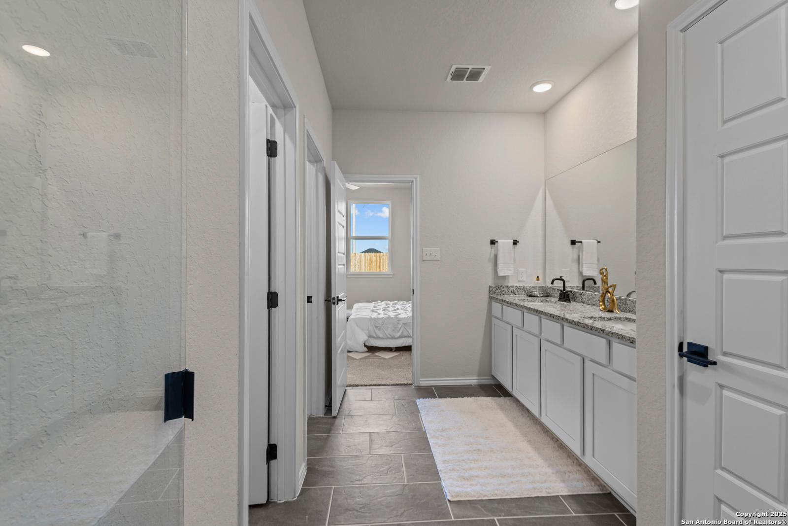 Modern master bathroom with dual vanities, gold faucets, glass shower, and bedroom view in Davidson Homes The Douglas C, Seguin, Texas