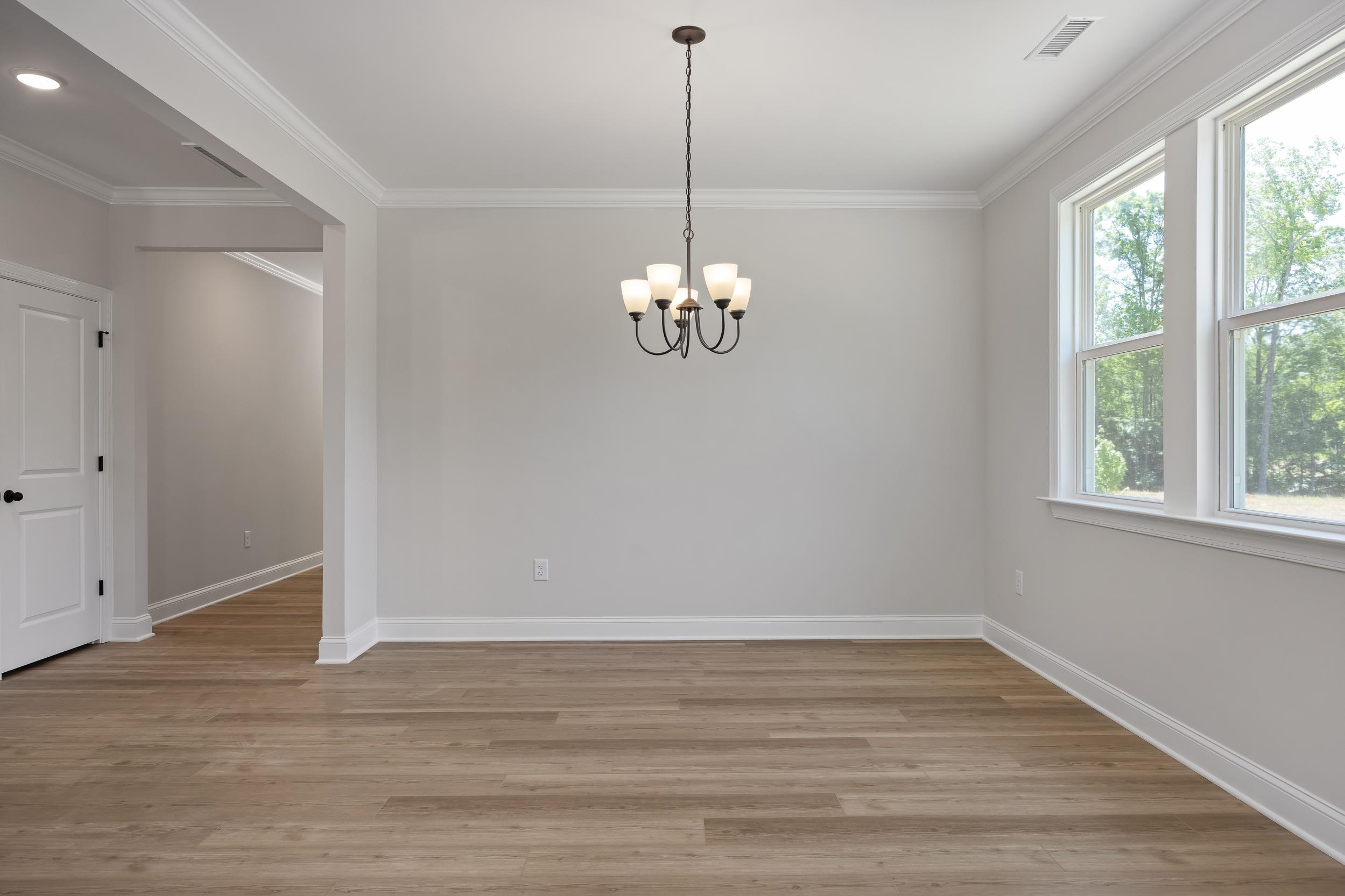 Spacious dining room in The Beech A with hardwood floors, elegant four-light chandelier, and large windows overlooking trees