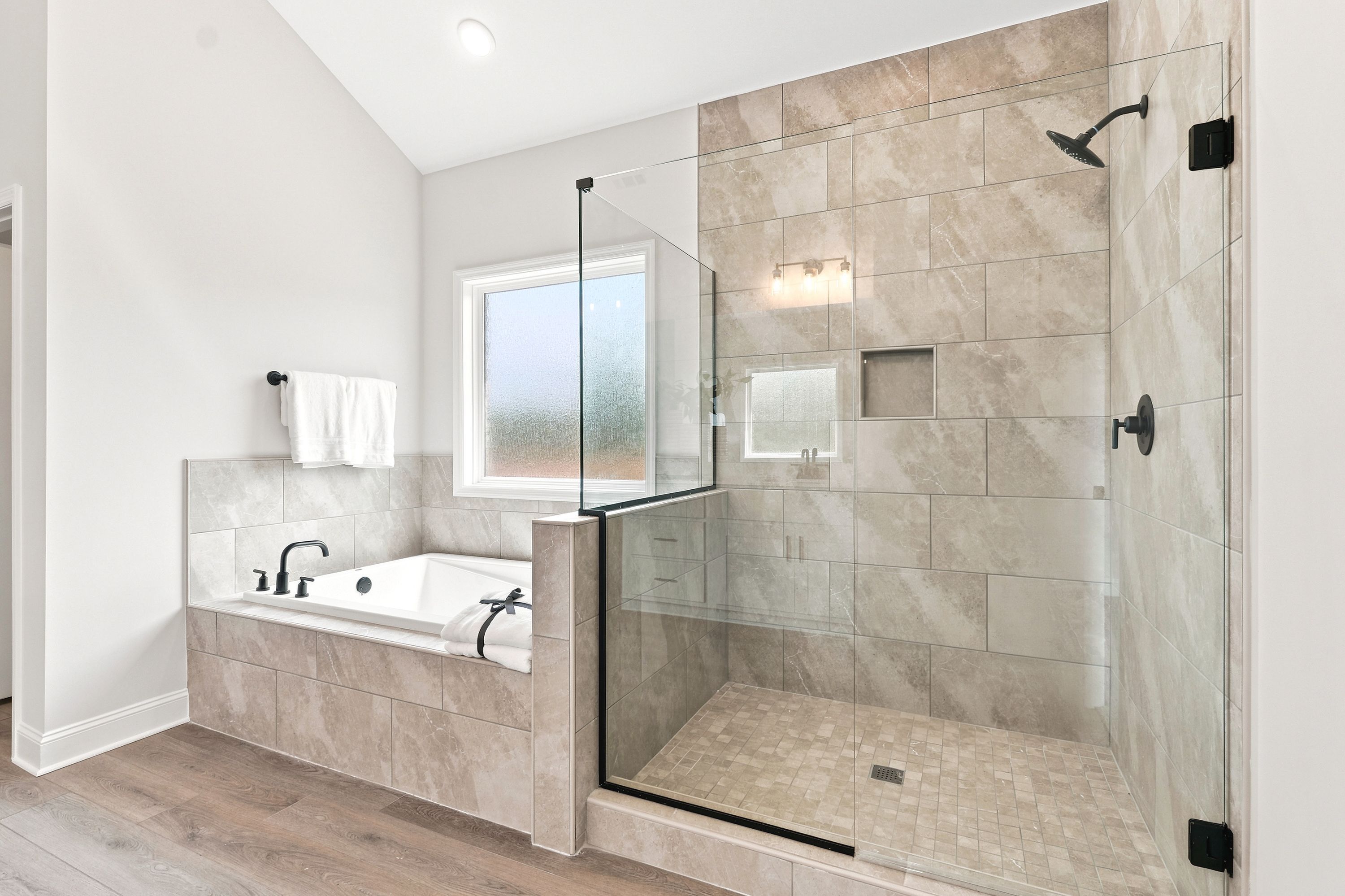 Modern primary bathroom at Riverton Preserve in Huntsville, AL with tiled soaking tub and glass-enclosed walk-in shower.