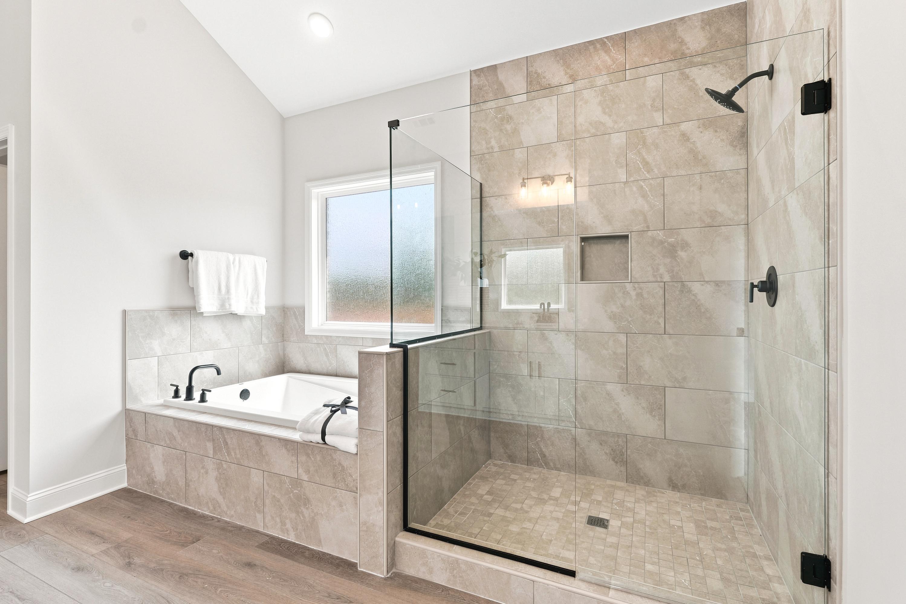 Modern primary bathroom at Riverton Preserve in Huntsville, AL with tiled soaking tub and glass-enclosed walk-in shower.