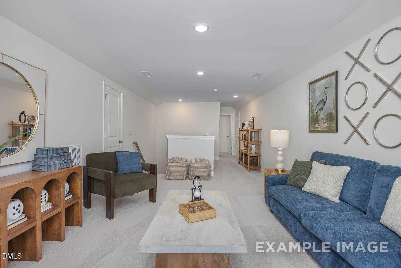 Cozy bonus room with blue sectional sofa, wooden console, round mirror, and bird wall art in Davidson Homes The Hickory II C, Wake Forest