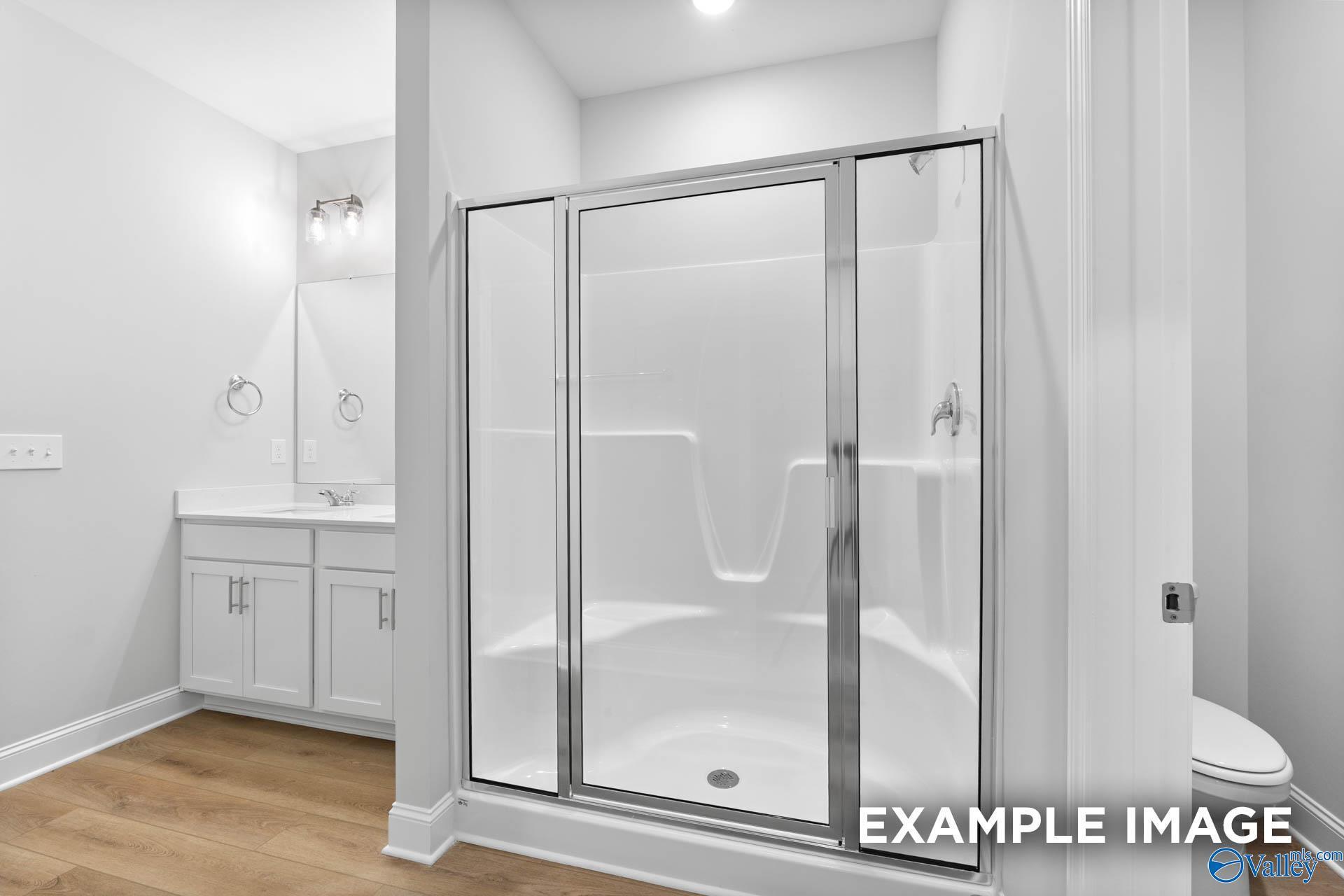 Modern white bathroom with glass shower enclosure, single vanity sink, and toilet in Davidson Homes The Daphne, Meridianville, AL