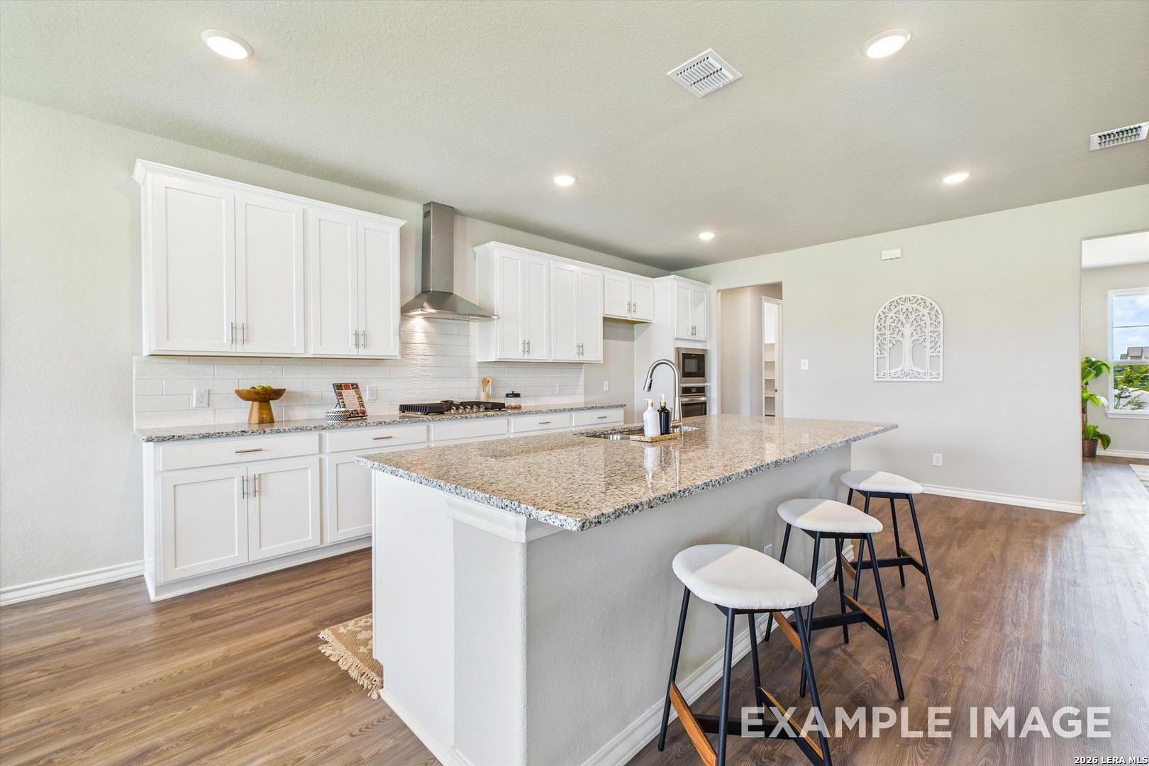 Modern kitchen with white cabinets, granite island, and bar seating in The Foster F floor plan at Potranco Oaks, TX.