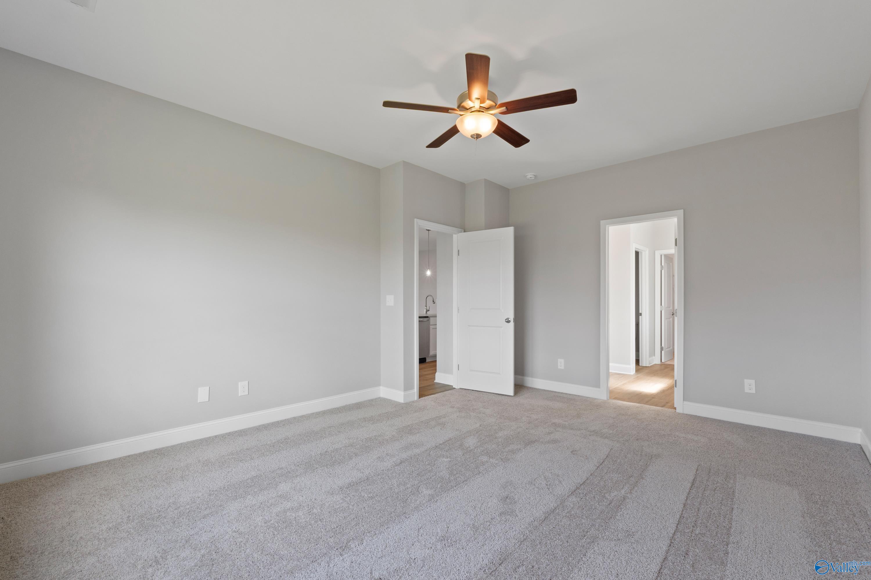 Spacious empty master bedroom with gray walls, carpet floor, ceiling fan, and en-suite bath door in Davidson Homes Everett B, Toney, AL