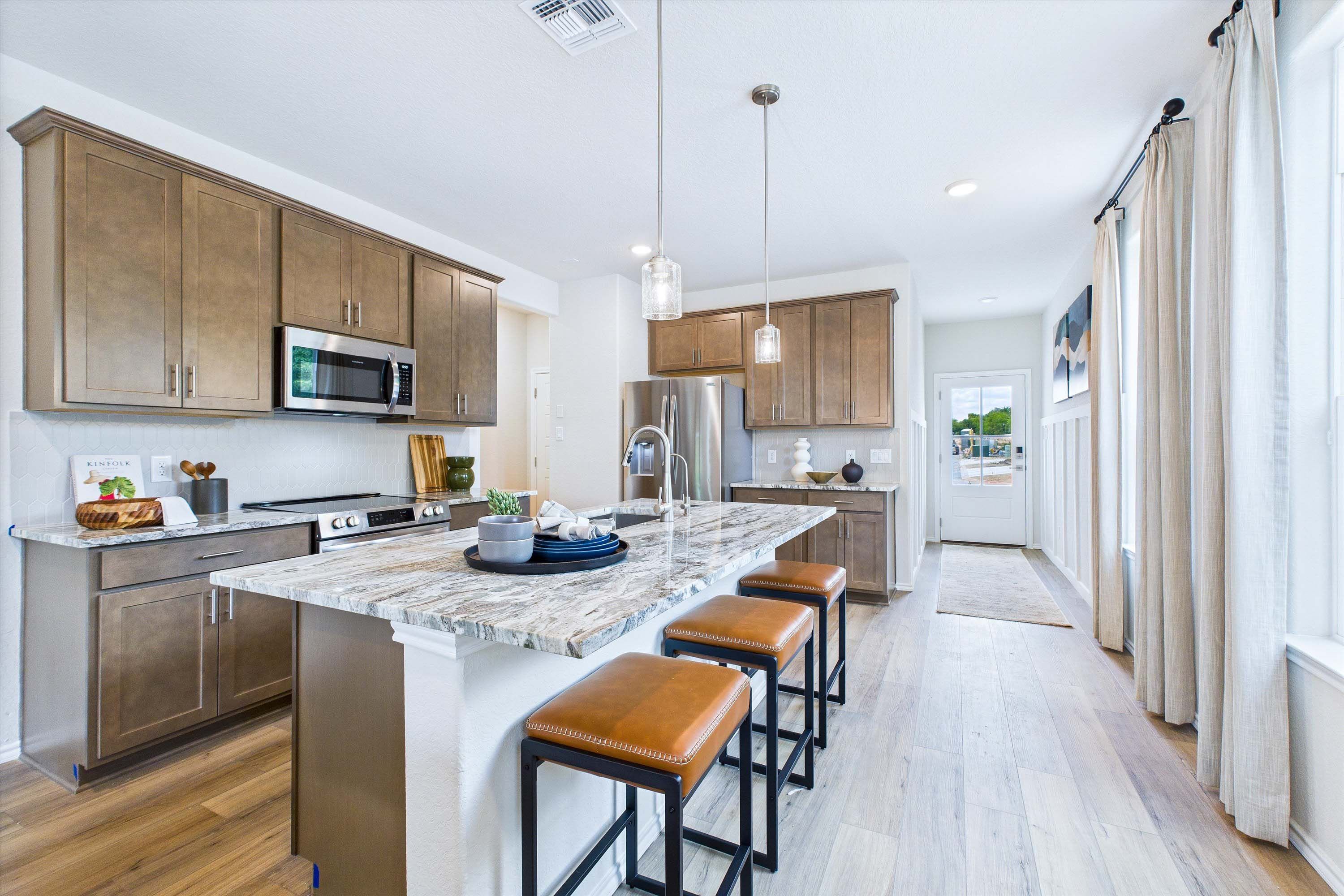 Modern kitchen in The Gillian C featuring a large stone island, leather bar stools, and warm wood cabinetry.