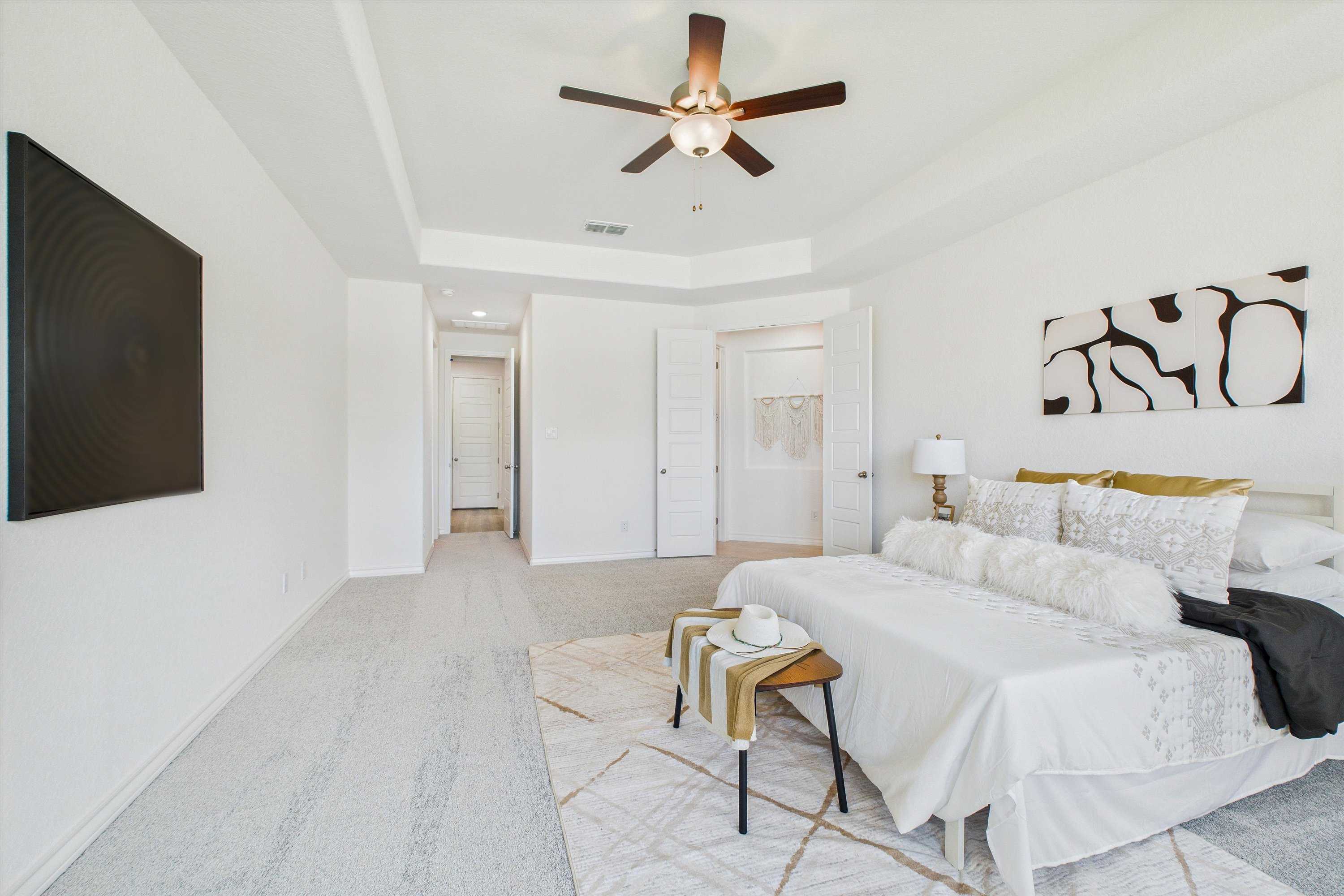 Elegant master bedroom with tray ceiling, ceiling fan, king bed, wall TV, and walk-in closet in Davidson Homes The Summerlin C, Castroville, TX