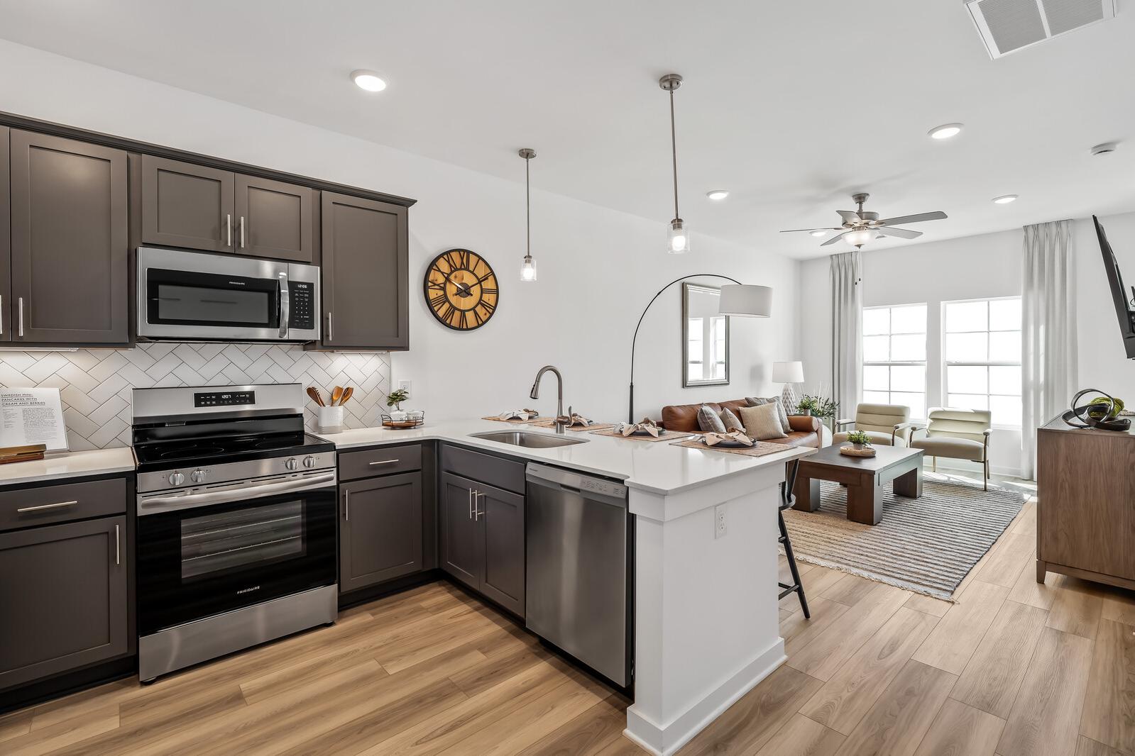 Open-concept kitchen and living room at The Towns at Red River in Gallatin, TN featuring gray cabinets, stainless steel appliances, and hardwood floors
