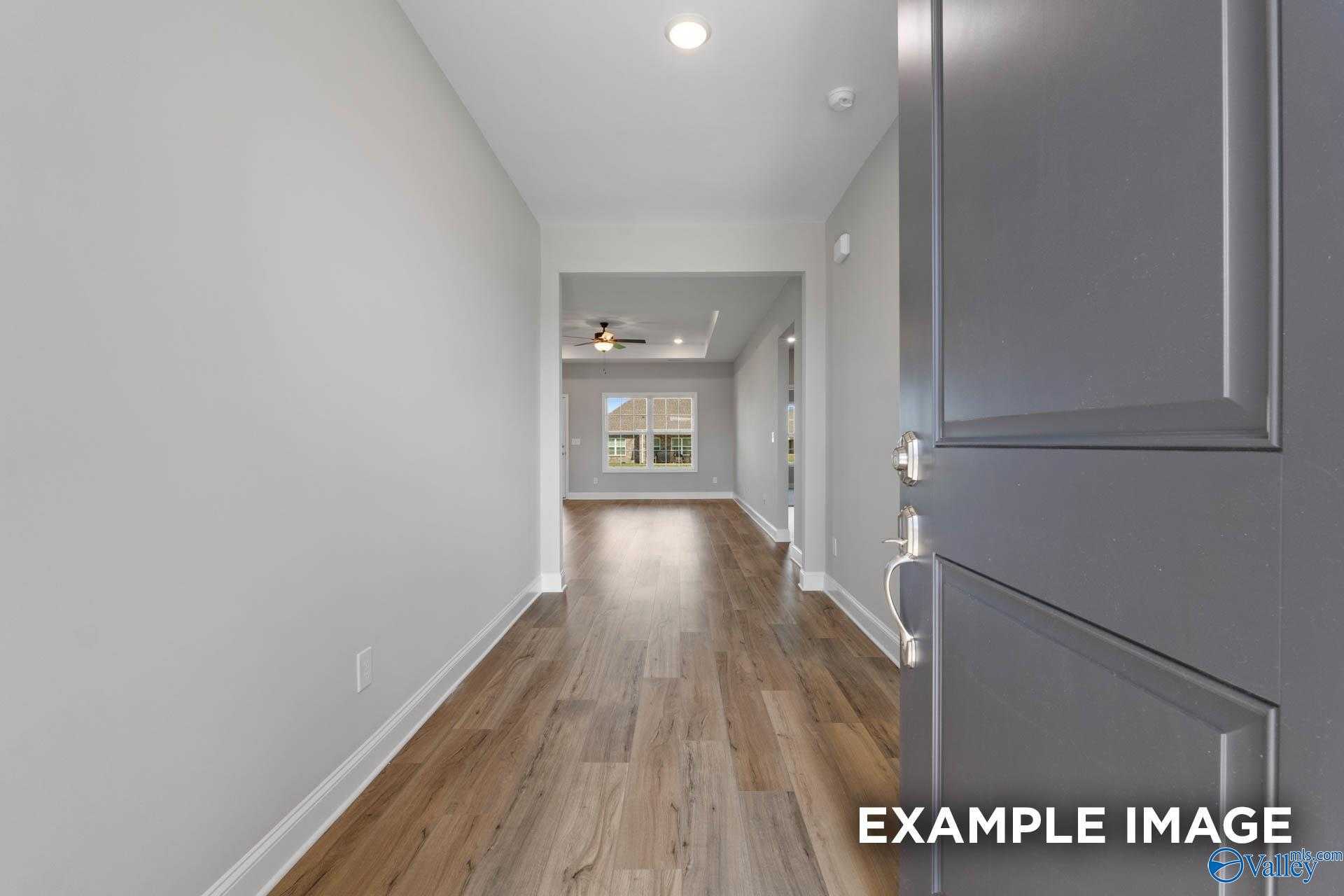 Spacious hallway with light hardwood floors, gray door, and natural light in The Montgomery B 3-bedroom home, Hartselle, Alabama