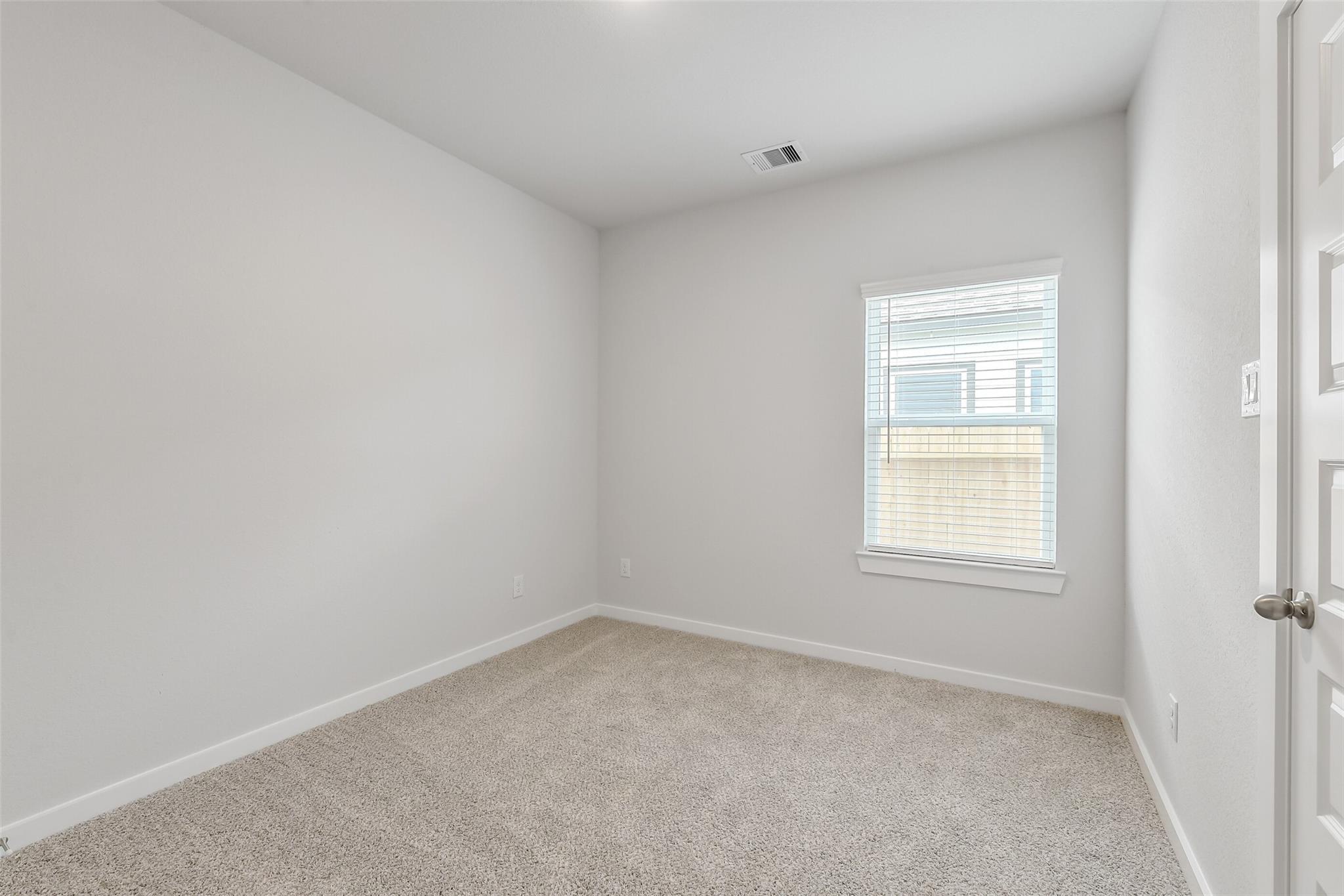 Bright empty bedroom featuring beige carpet, white walls, and window blinds in Davidson Homes San Marcos E, Conroe TX