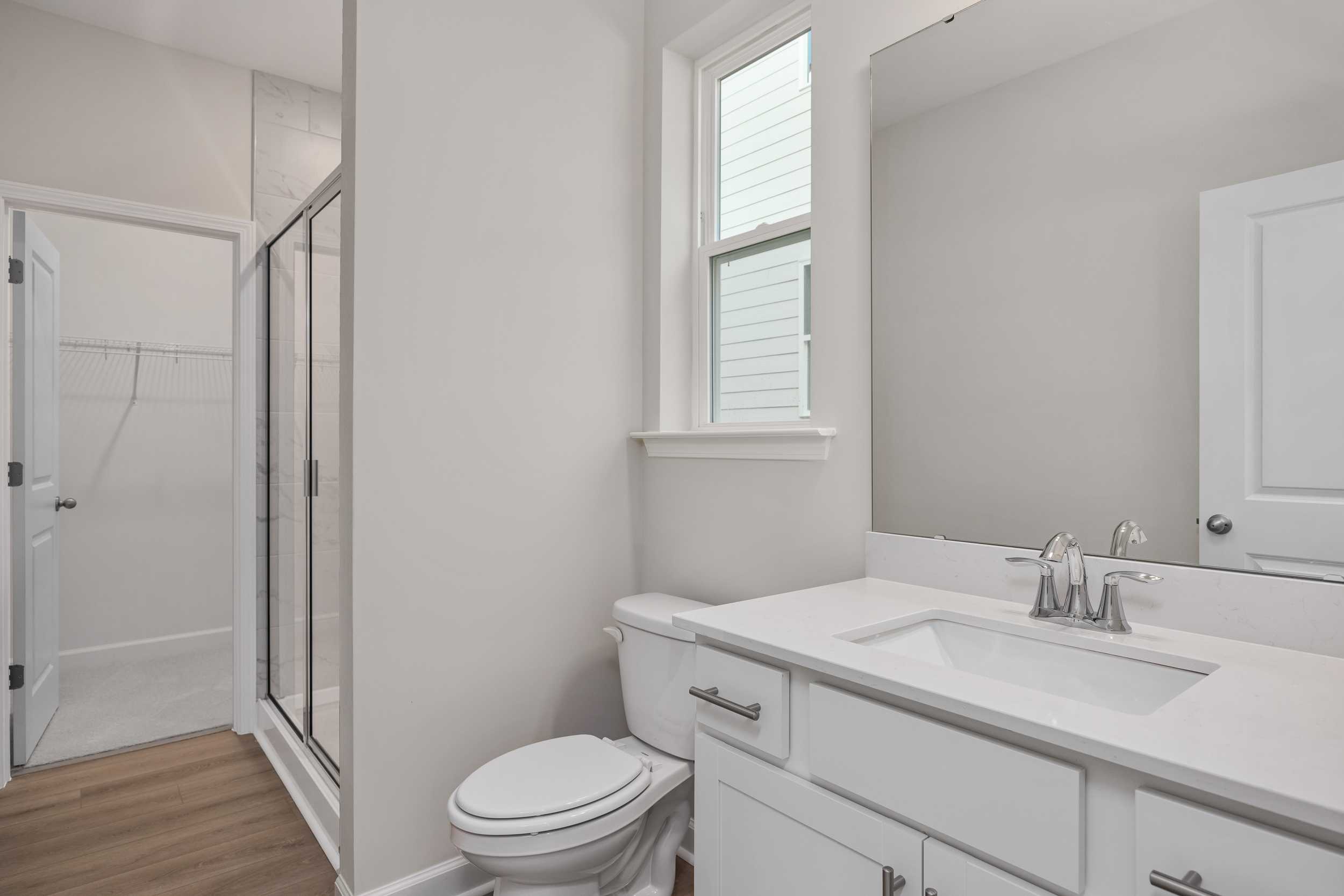 Modern master bathroom in The Aspen C with glass walk-in shower, white vanity sink, toilet, and window by Davidson Homes