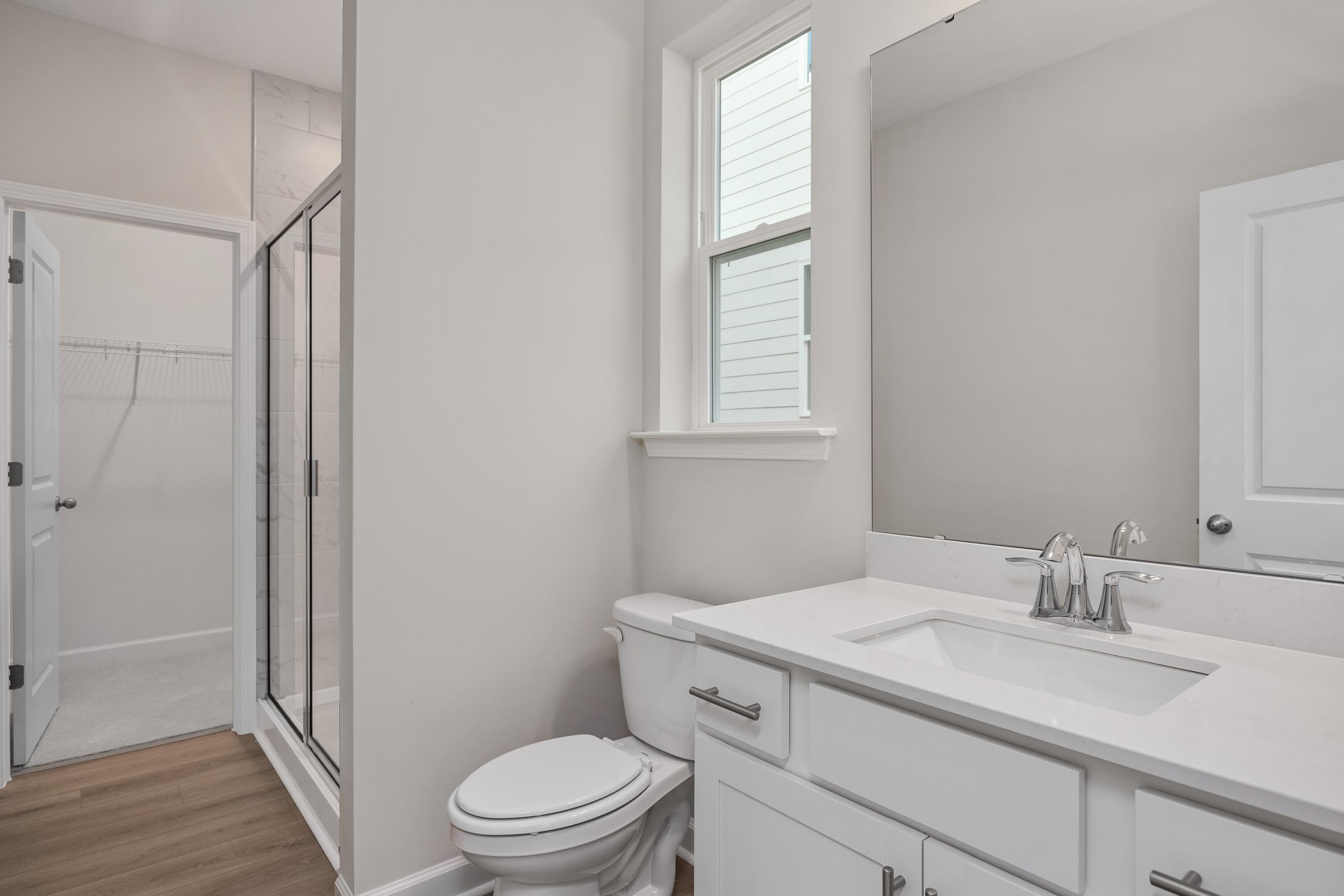 Modern master bathroom in The Aspen C with glass walk-in shower, white vanity sink, toilet, and window by Davidson Homes