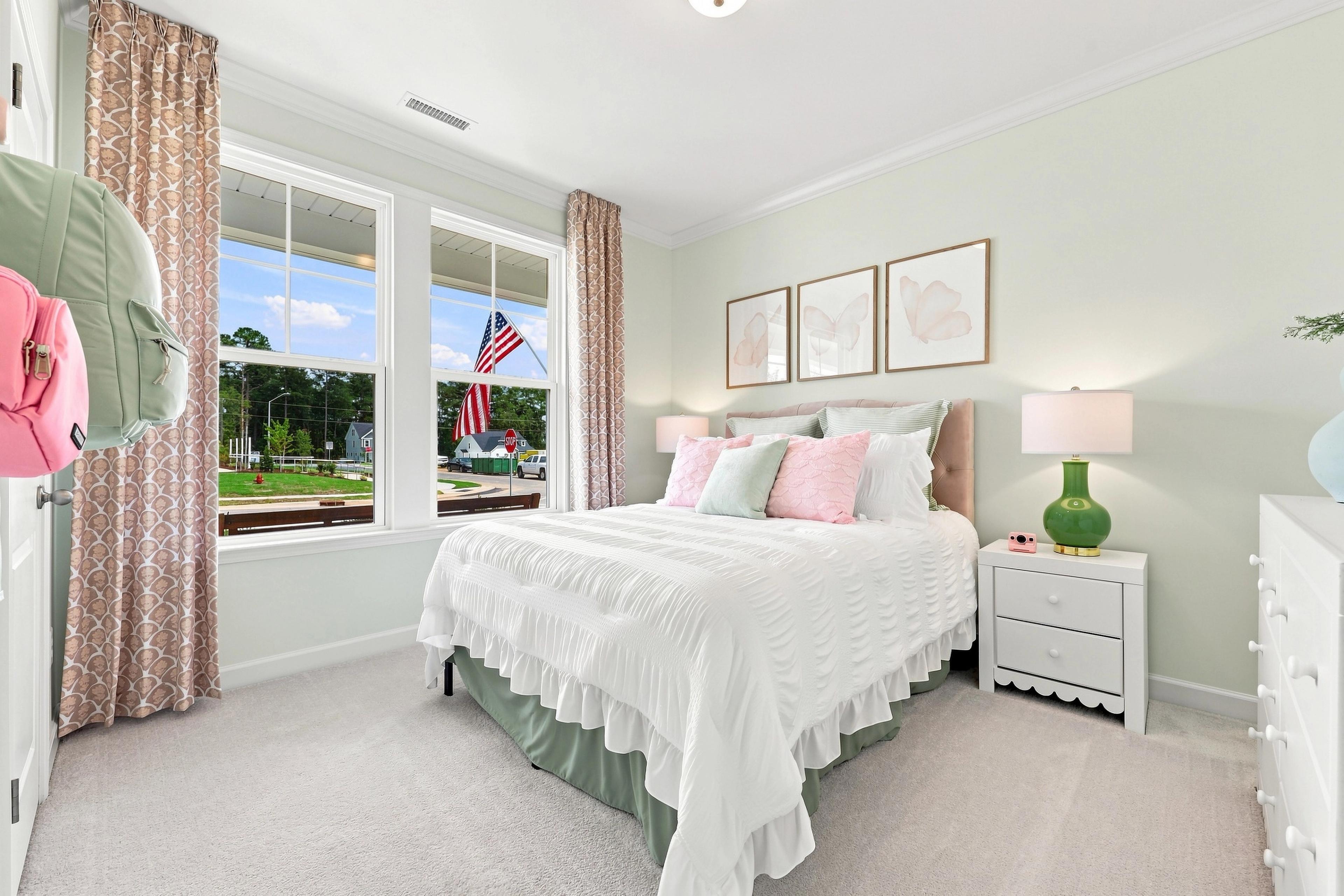 Bright and airy bedroom in The Daphne home design featuring soft pastel decor, white bedding, and large windows.