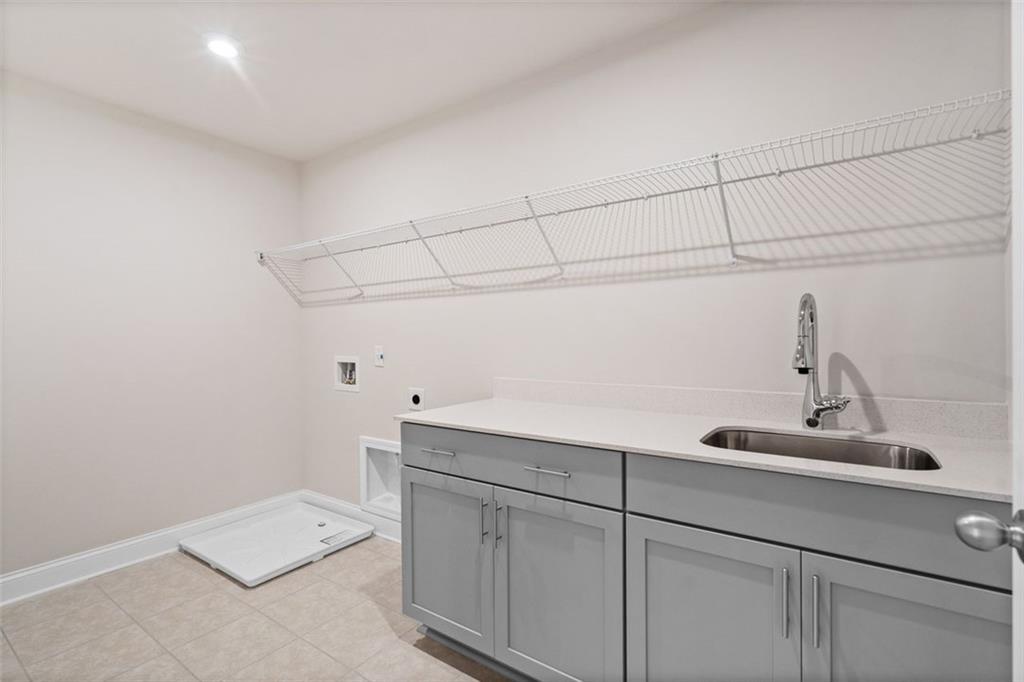 Modern laundry room featuring washer, dryer, utility sink and gray cabinets in Davidson Homes The Hickory B at Wehunt Meadows, Hoschton