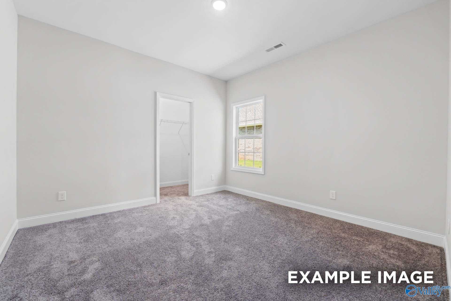 Bright bedroom with gray carpet, light walls, closet door and window in The Lanier home by Davidson Homes, Meridianville, AL