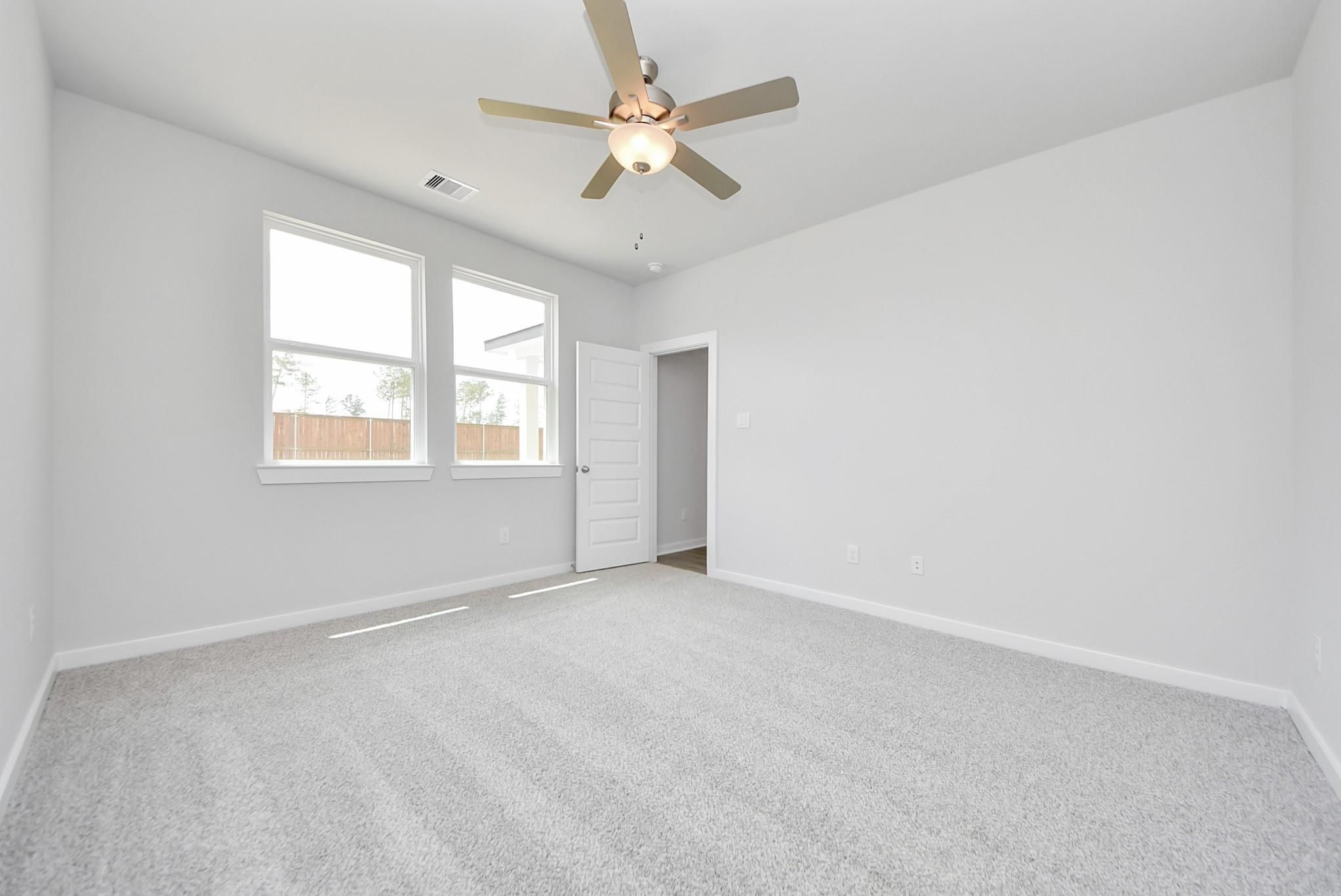 Bright, carpeted bedroom with ceiling fan in The Blanco F floor plan at Spring Branch Crossing, Conroe, Texas.