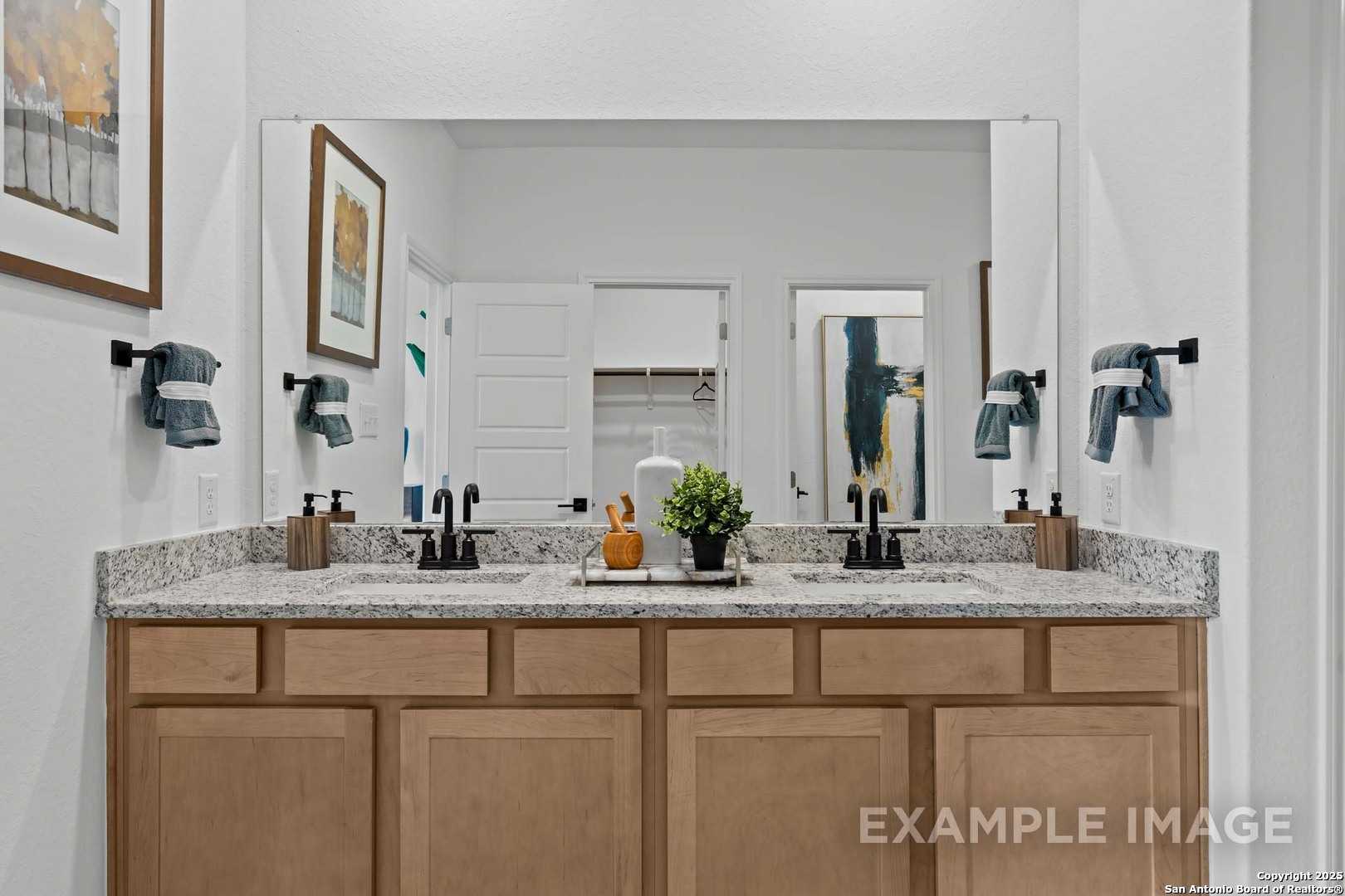 Modern master bathroom featuring double granite vanity, oak cabinets, mirrors, and artwork in Davidson Homes The Douglas C, Seguin, Texas