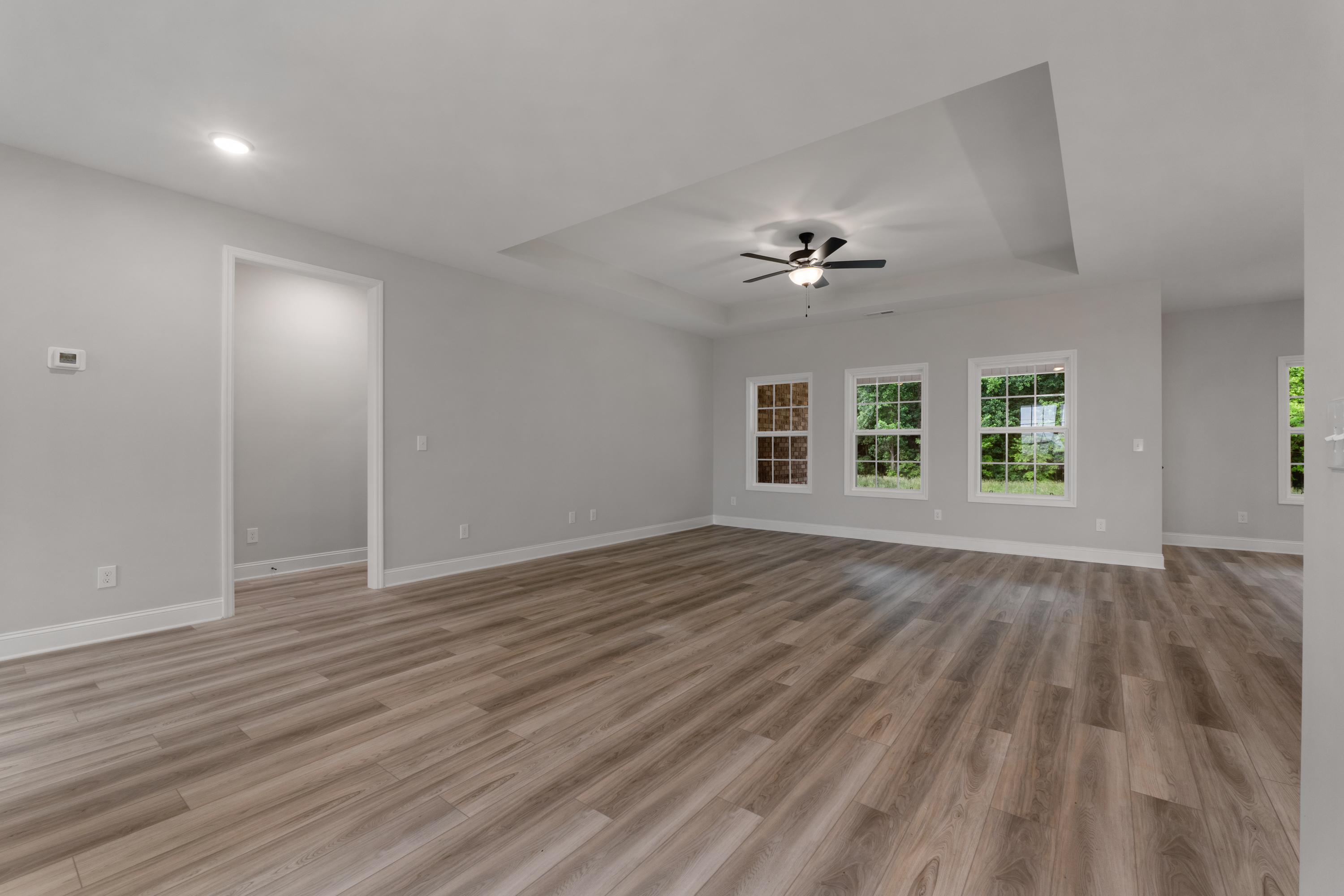 Spacious open living area in The Oxford home by Davidson Homes with tray ceiling fan, large windows, gray walls, and hardwood-style floors