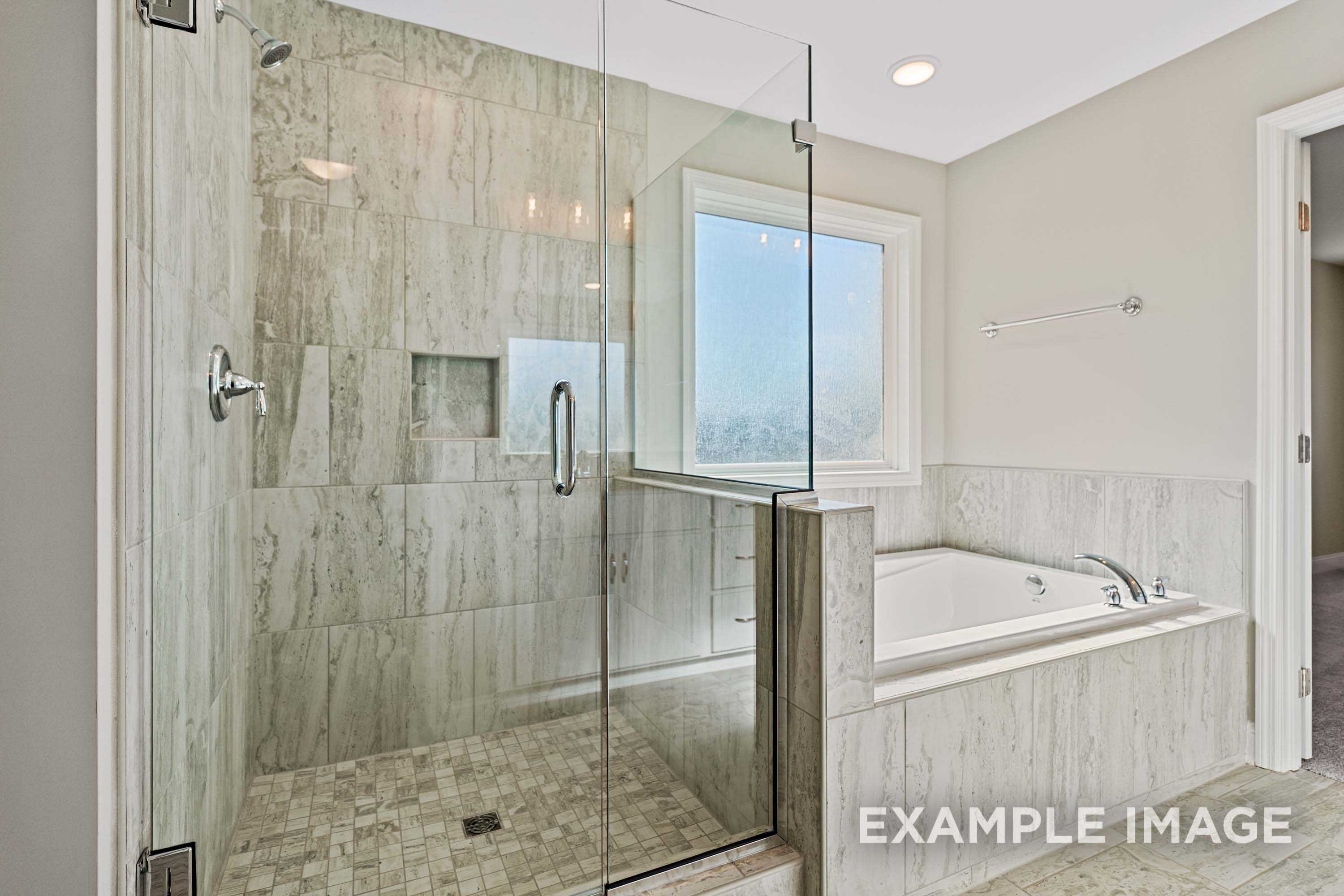 Luxurious master bathroom in The Madison A with frameless glass shower, soaking tub, and tiled accents