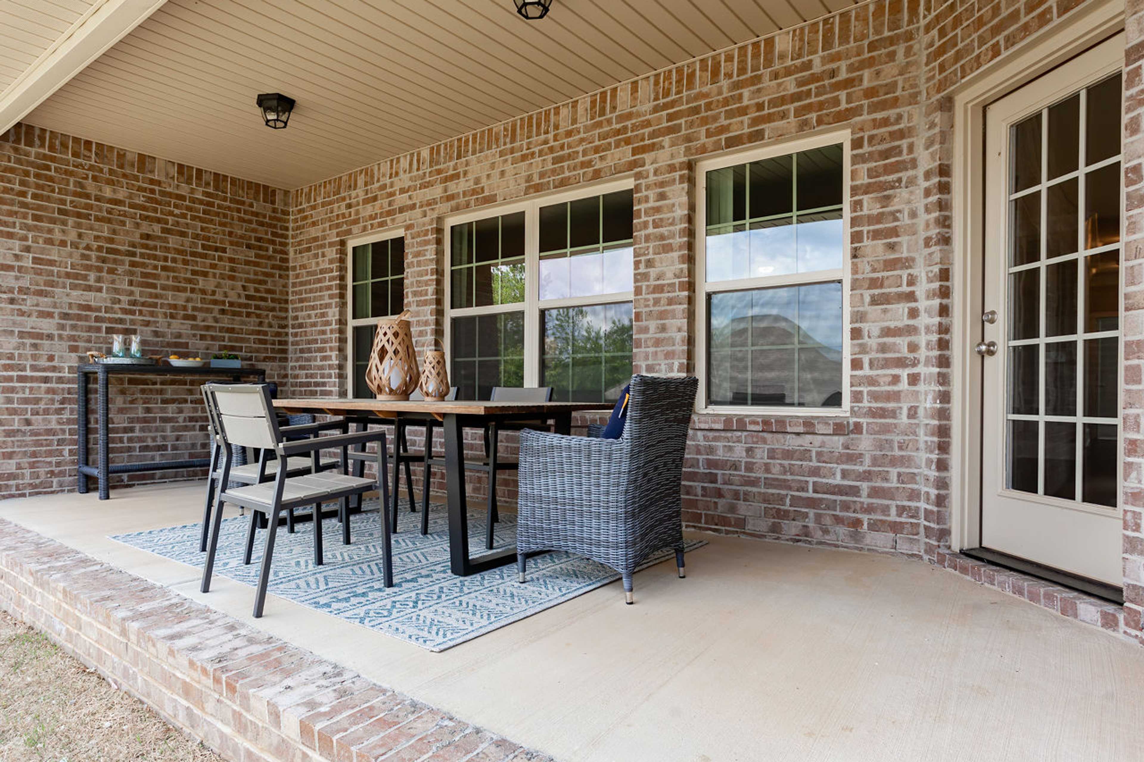 Covered patio at Laurenwood Preserve in Madison Alabama with light brick walls, wooden dining table, wicker chairs, and large windows