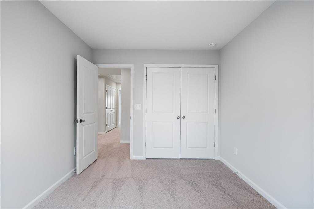 Bright secondary bedroom with light gray walls, beige carpet, and double-door closet in Davidson Homes The Durant A, Emerson, Georgia
