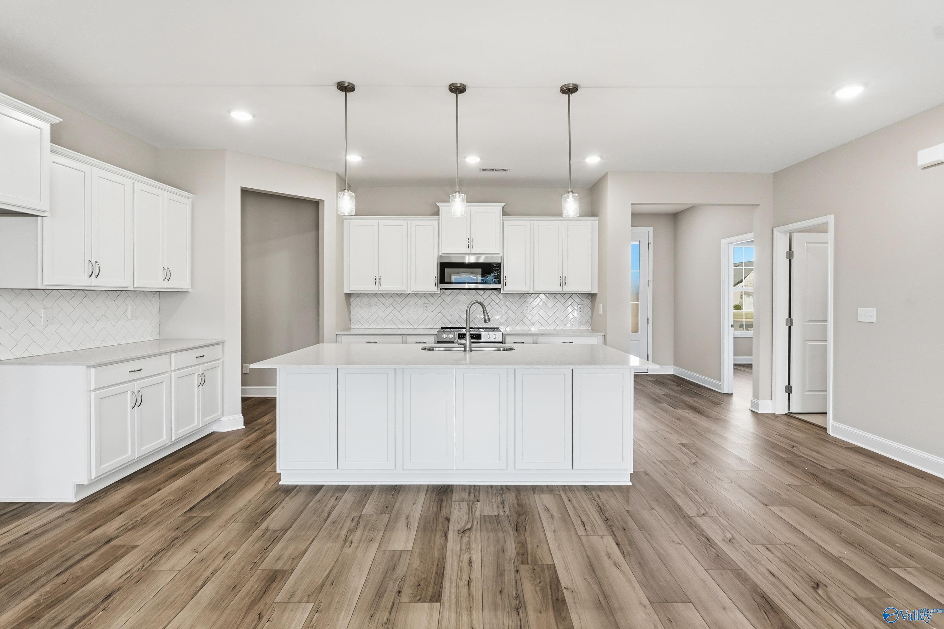 Modern white kitchen featuring large island, subway tile backsplash, and pendant lights in Davidson Homes The Lanier, Toney, Alabama