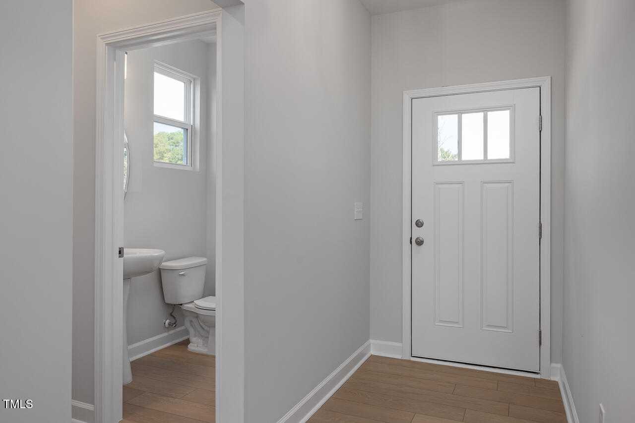 Bright powder room with white sink and toilet adjacent to entry foyer with glass front door in The Graham home, Fuquay-Varina, NC