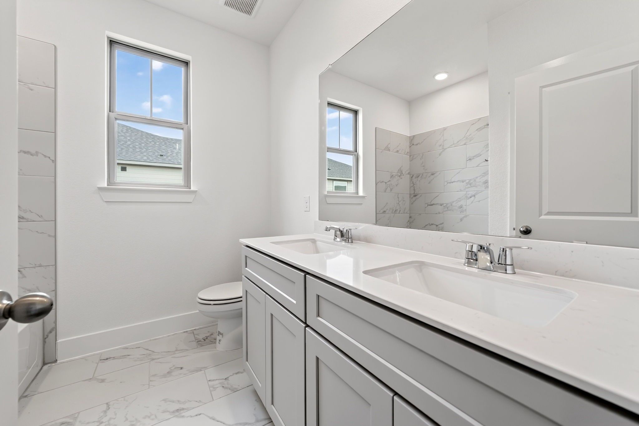 Bright bathroom with dual vanities, marble tile shower, and white cabinetry in Davidson Homes The Holly F, Josephine, Texas