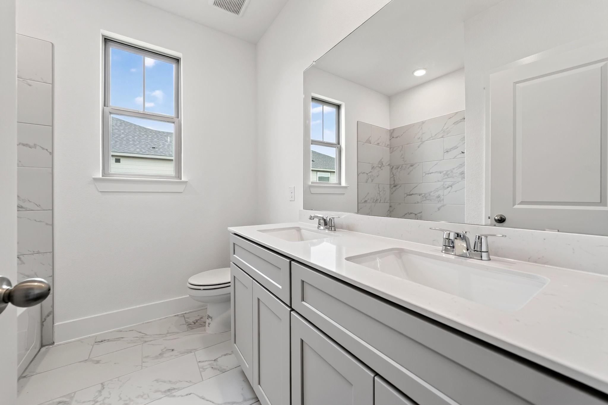 Bright bathroom with dual vanities, marble tile shower, and white cabinetry in Davidson Homes The Holly F, Josephine, Texas