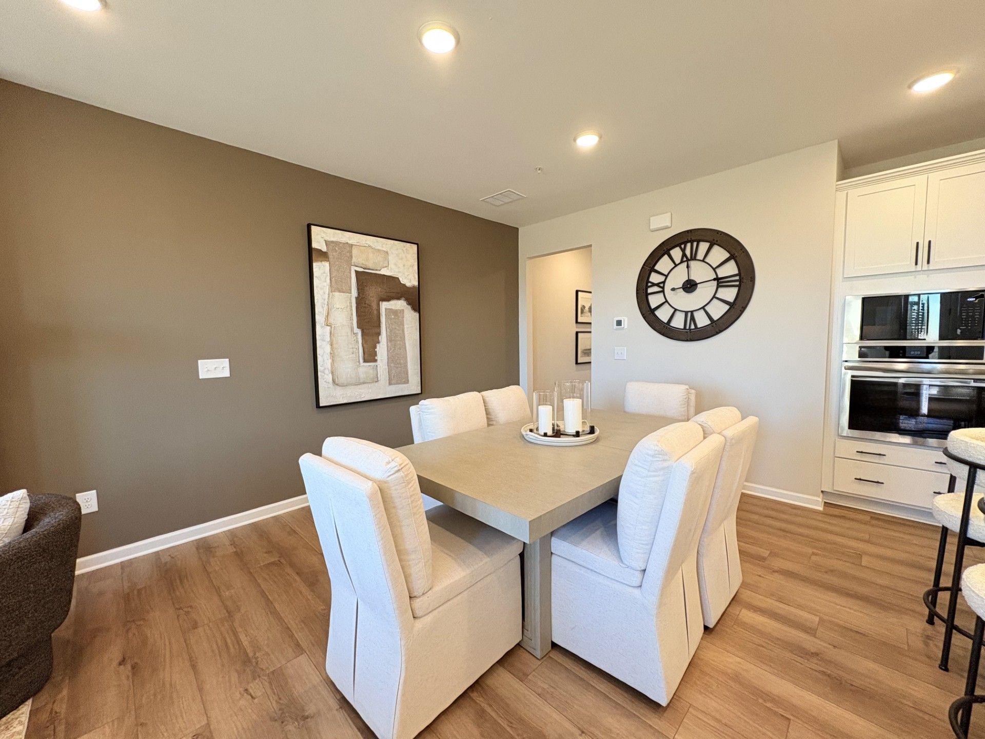 Spacious dining room in Hemingway community Cumming GA featuring white upholstered chairs round table abstract wall art large clock and open kitchen with hardwood floors