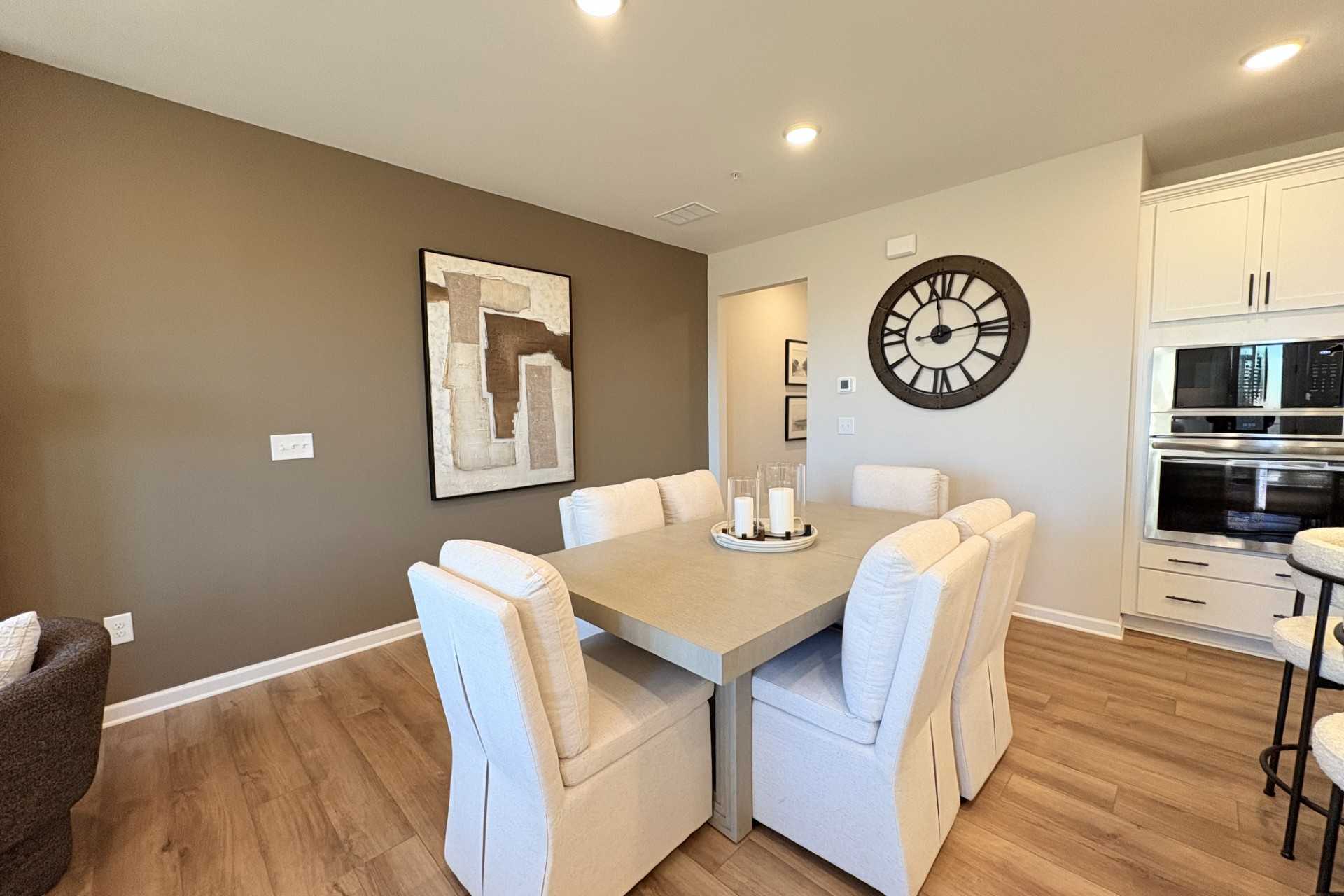 Spacious dining room in Hemingway community Cumming GA featuring white upholstered chairs round table abstract wall art large clock and open kitchen with hardwood floors