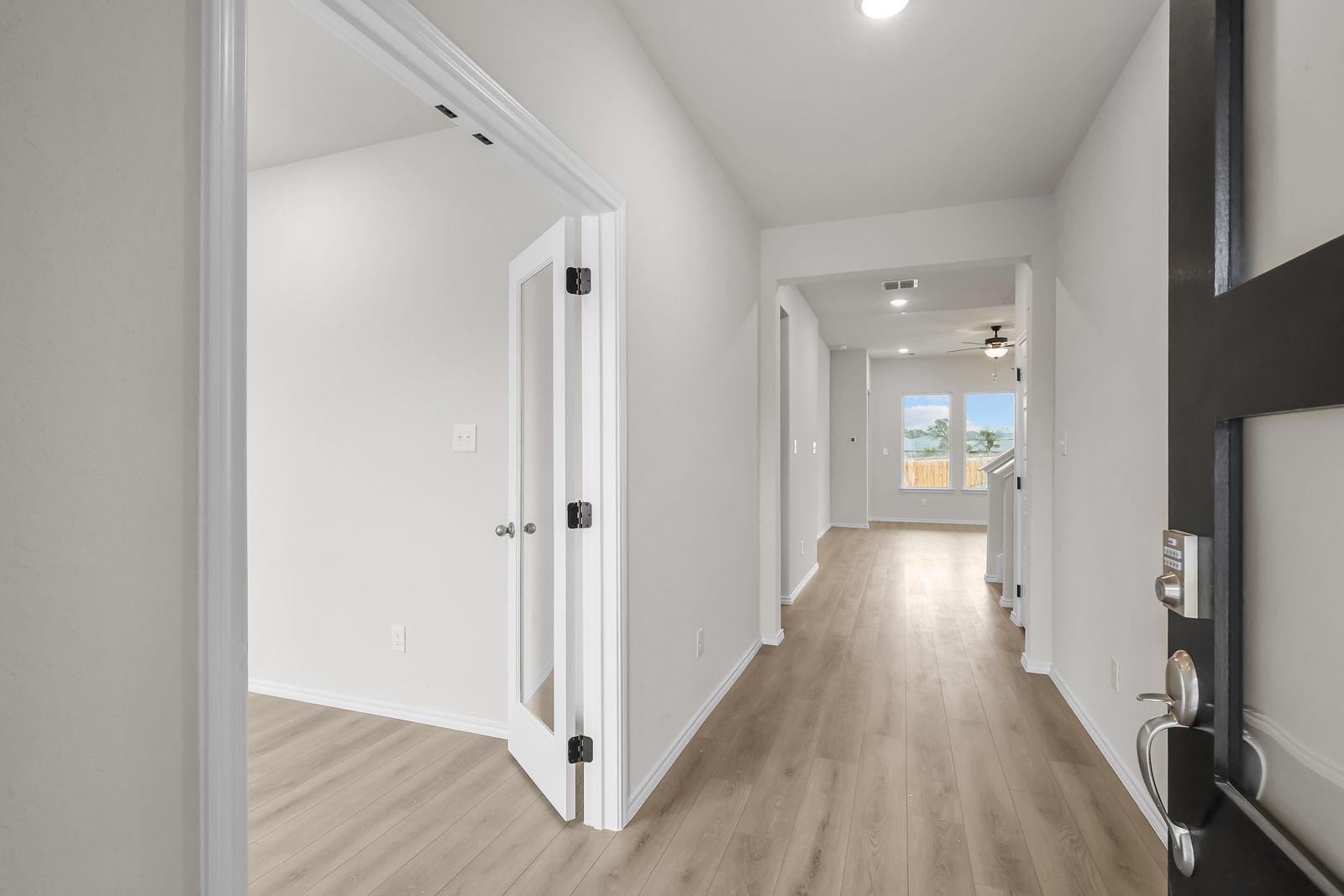 Bright foyer and entryway of The Sycamore B featuring modern wood-look flooring and a glass-paneled den door.