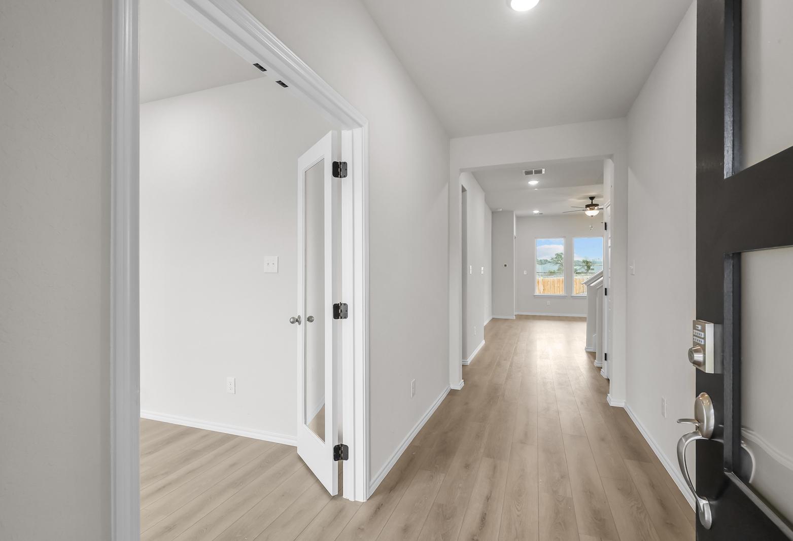 Bright foyer and entryway of The Sycamore B featuring modern wood-look flooring and a glass-paneled den door.