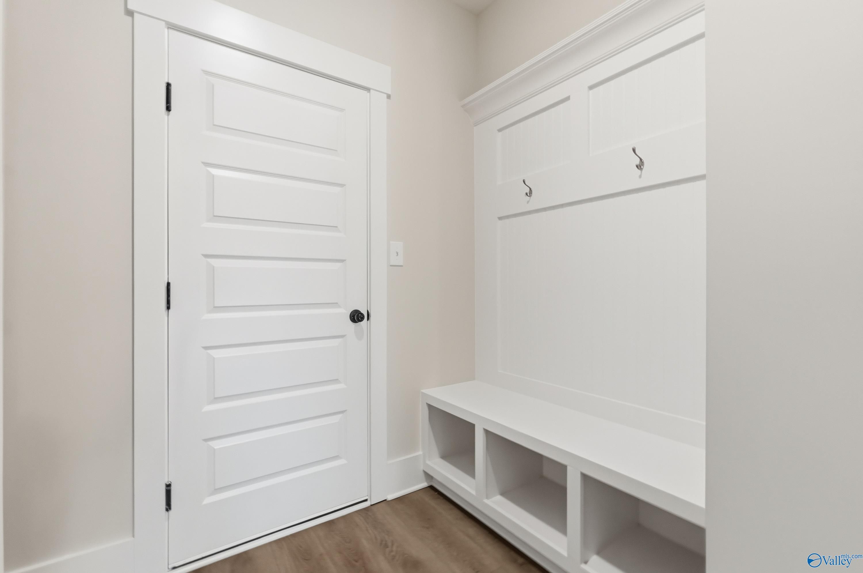 Spacious mudroom with white built-in bench, shelves, hooks, and paneled door in Davidson Homes The Finleigh, Meridianville, Alabama