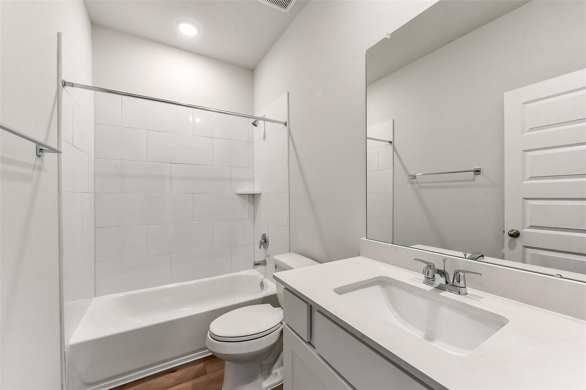 Bright white bathroom with subway tile tub-shower combo, quartz vanity, mirror in Davidson Homes The Costa C, Dayton Texas