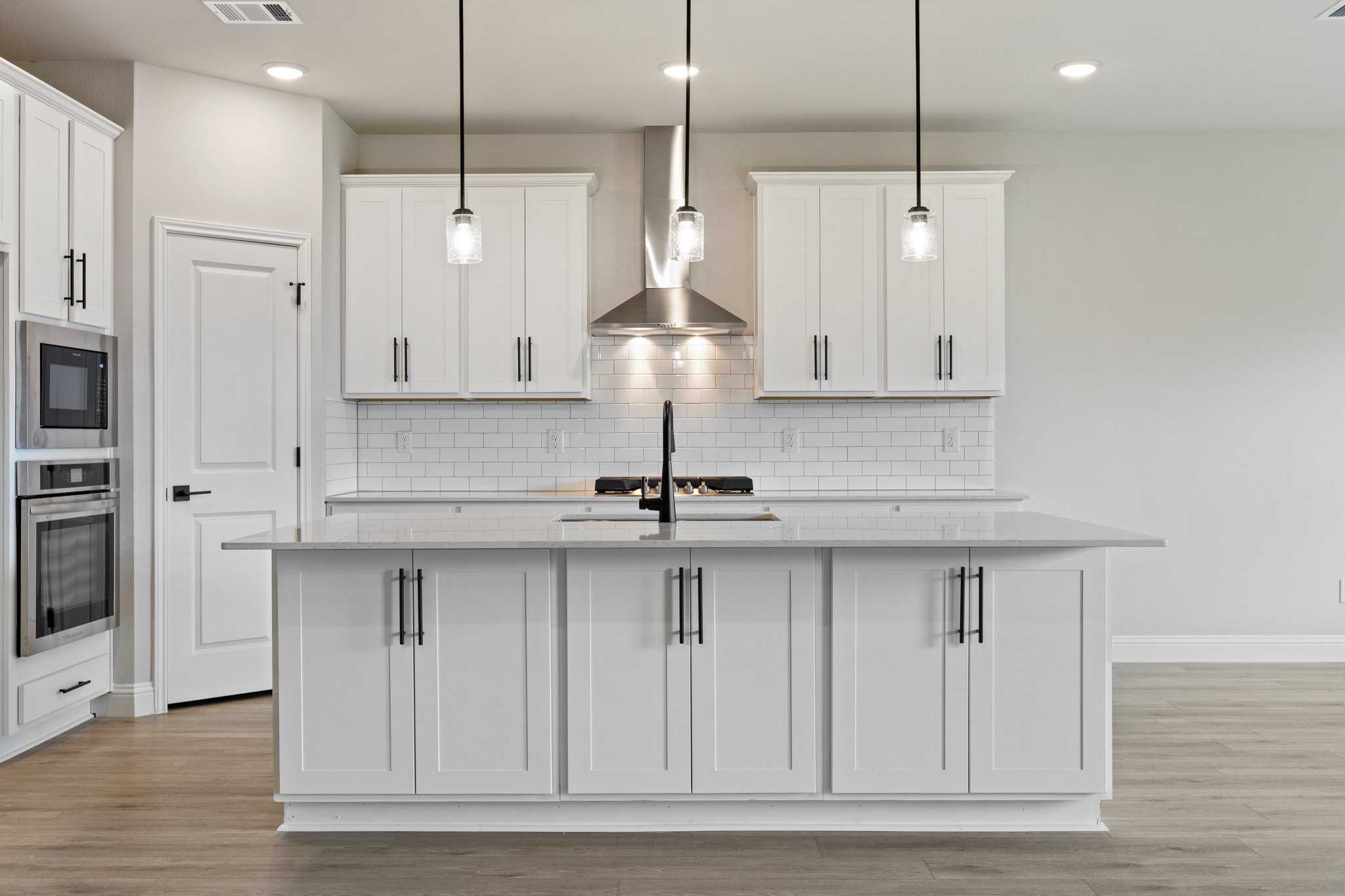 Modern white kitchen in The Harrison C by Davidson Homes featuring large center island, subway tile backsplash, and pendant lights