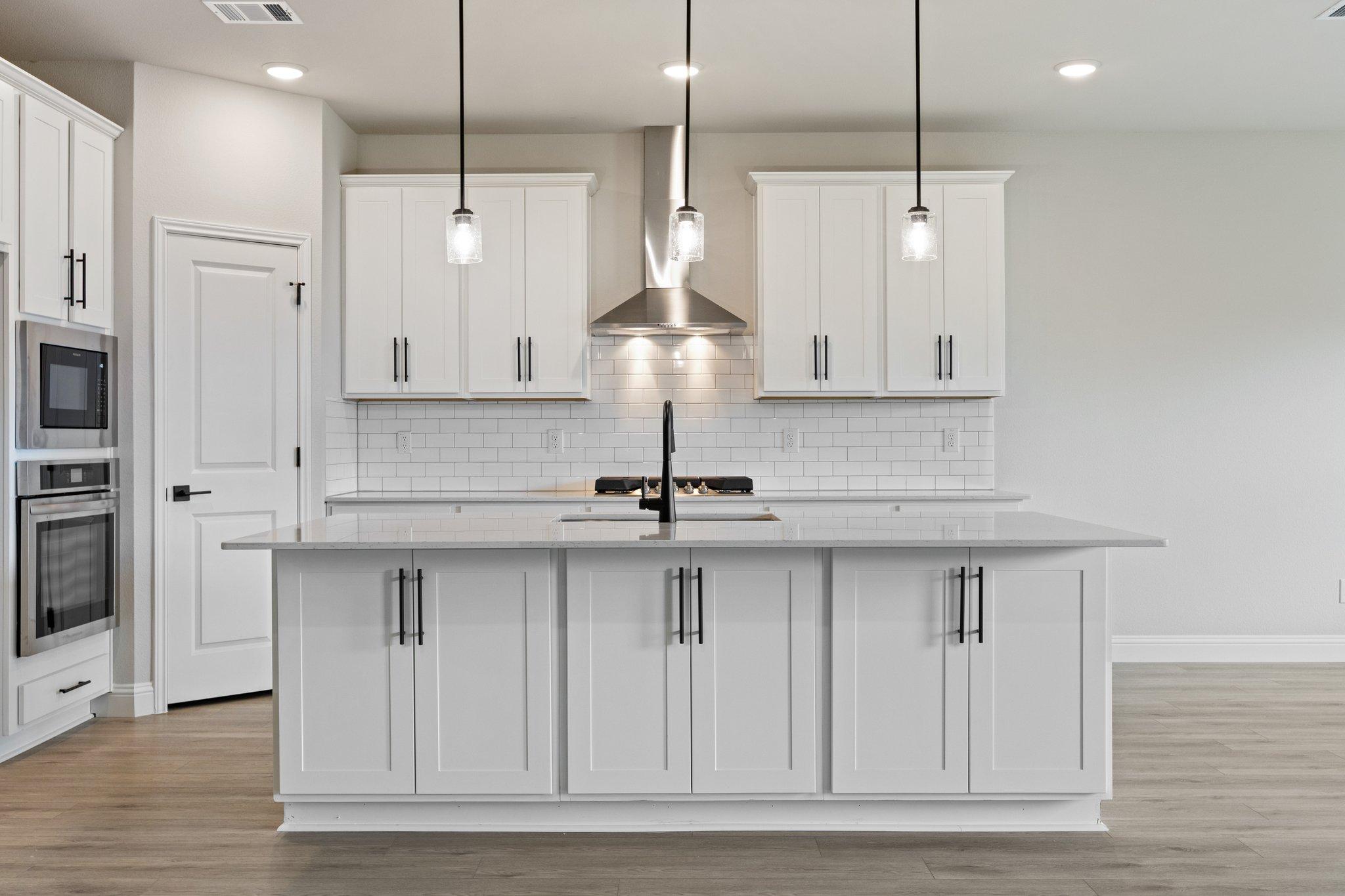 Spacious The Harrison kitchen with white shaker cabinets, large center island sink, stainless steel appliances, subway tile backsplash