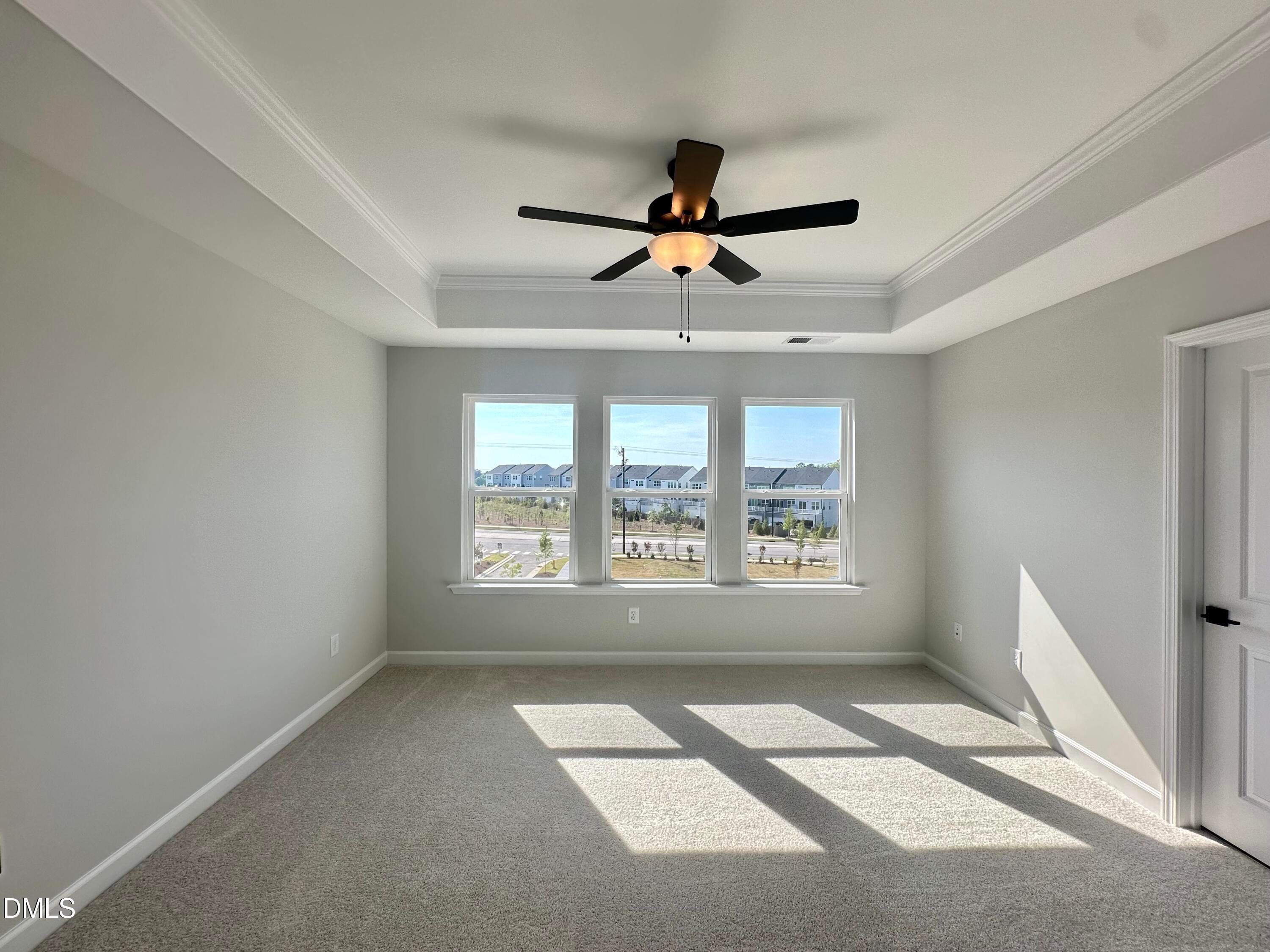 Bright bedroom with light gray walls, ceiling fan, three large windows overlooking neighborhood, and carpeted floor in Davidson Homes The Avery, Knightdale, NC
