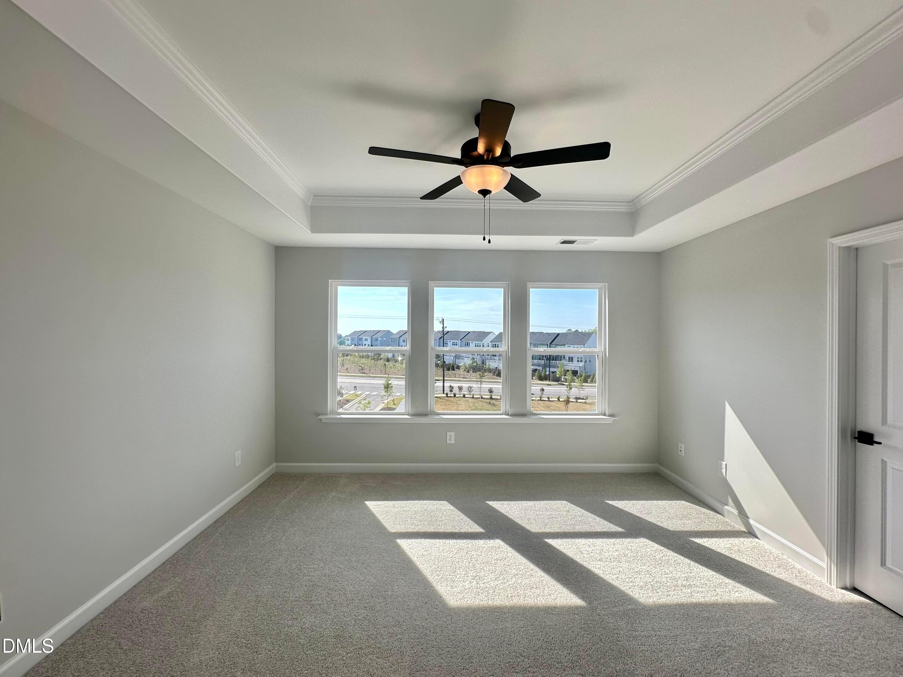 Bright bedroom with light gray walls, ceiling fan, three large windows overlooking neighborhood, and carpeted floor in Davidson Homes The Avery, Knightdale, NC