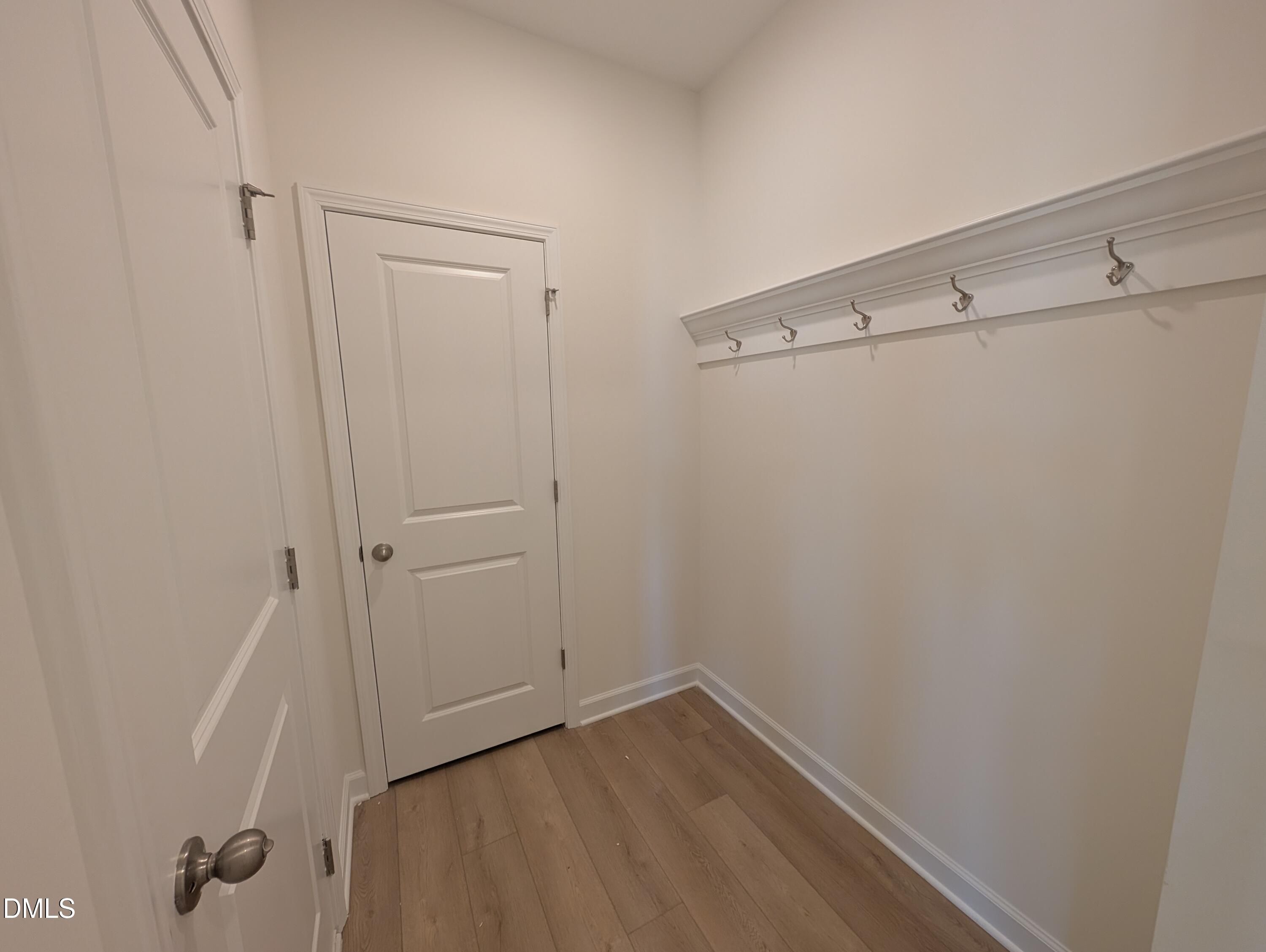 Mudroom with wall-mounted coat hooks, white doors, and wood-look flooring in Davidson Homes The Magnolia A, Wendell Ridge, NC