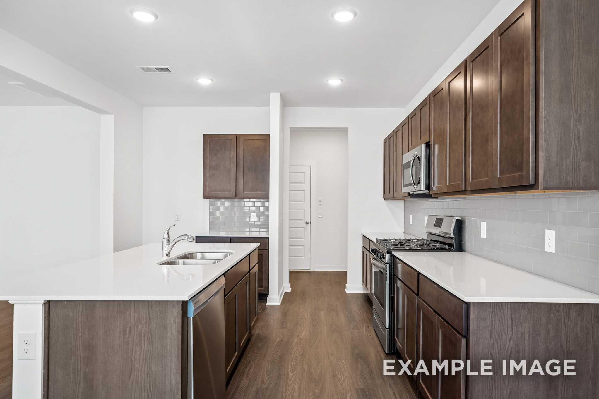 Spacious modern kitchen in The Grayson C with white quartz island, espresso cabinets, subway tile backsplash, and stainless steel appliances