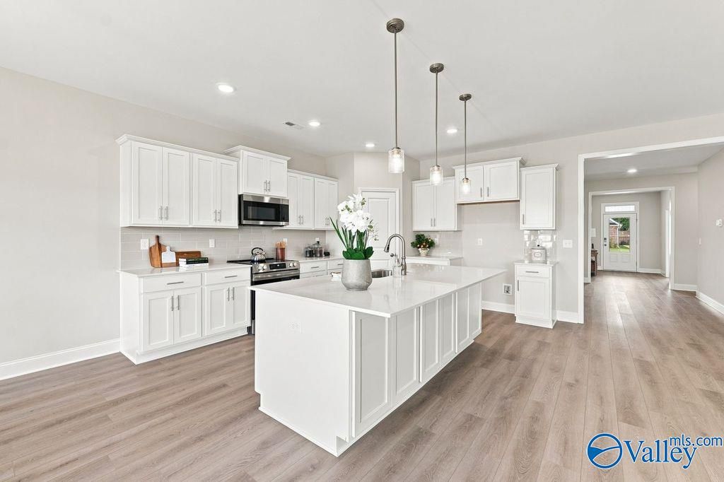 White kitchen with large island, pendant lights, and hardwood floors in Davidson Homes The Harrison floor plan, Hartselle, AL
