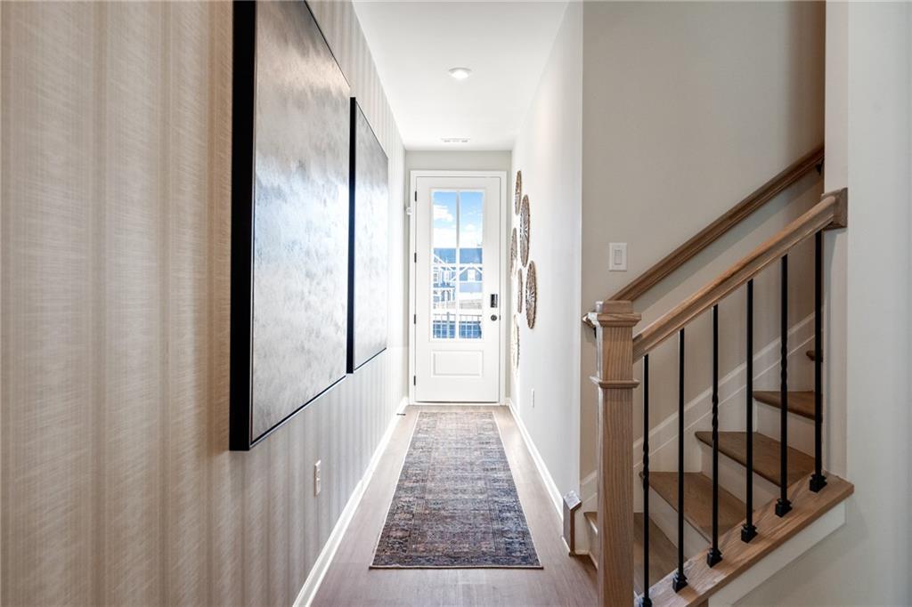 Elegant foyer hallway with abstract wall art, white glass-paneled door, runner rug, and oak staircase in Davidson Homes The Cary C, Winder GA