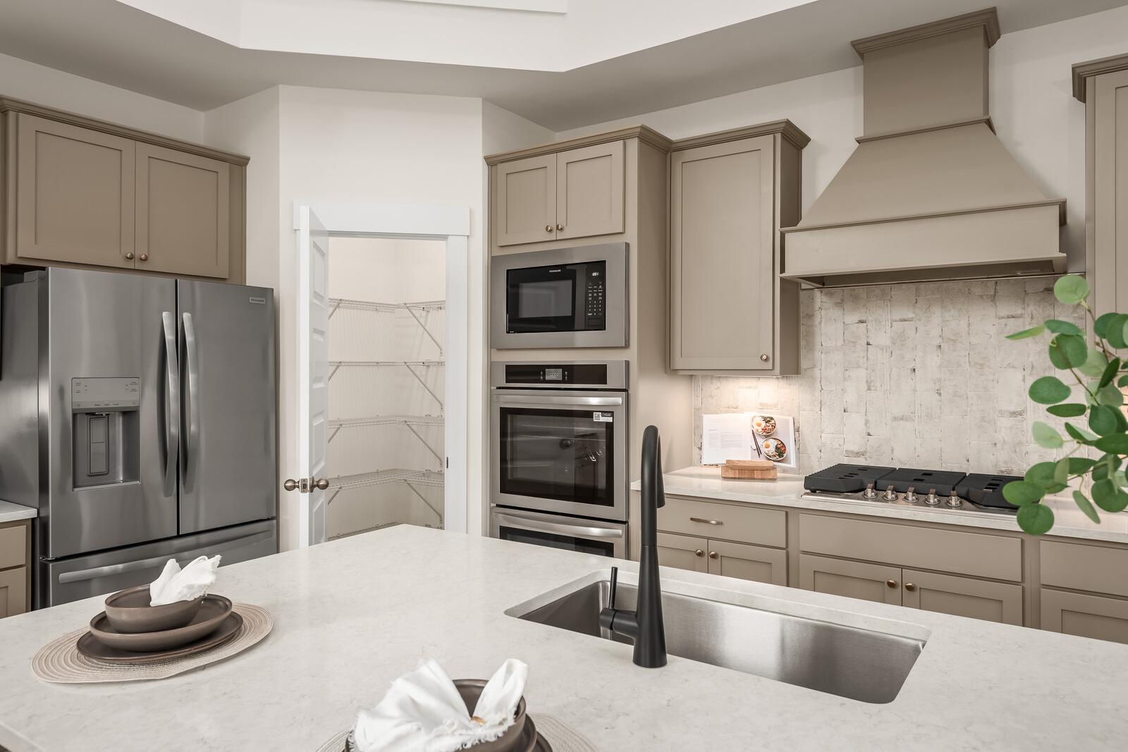 Spacious Ridgeport kitchen with taupe shaker cabinets, stainless steel fridge, double ovens, gas range, and large island sink in Mt. Juliet home