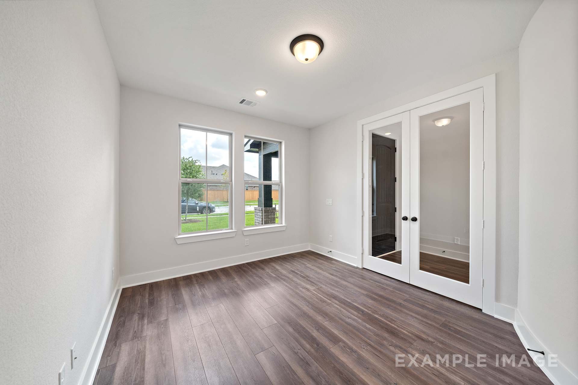 Bright flexible room in The Victoria by Davidson Homes with wood-look flooring, glass French doors, and large windows.