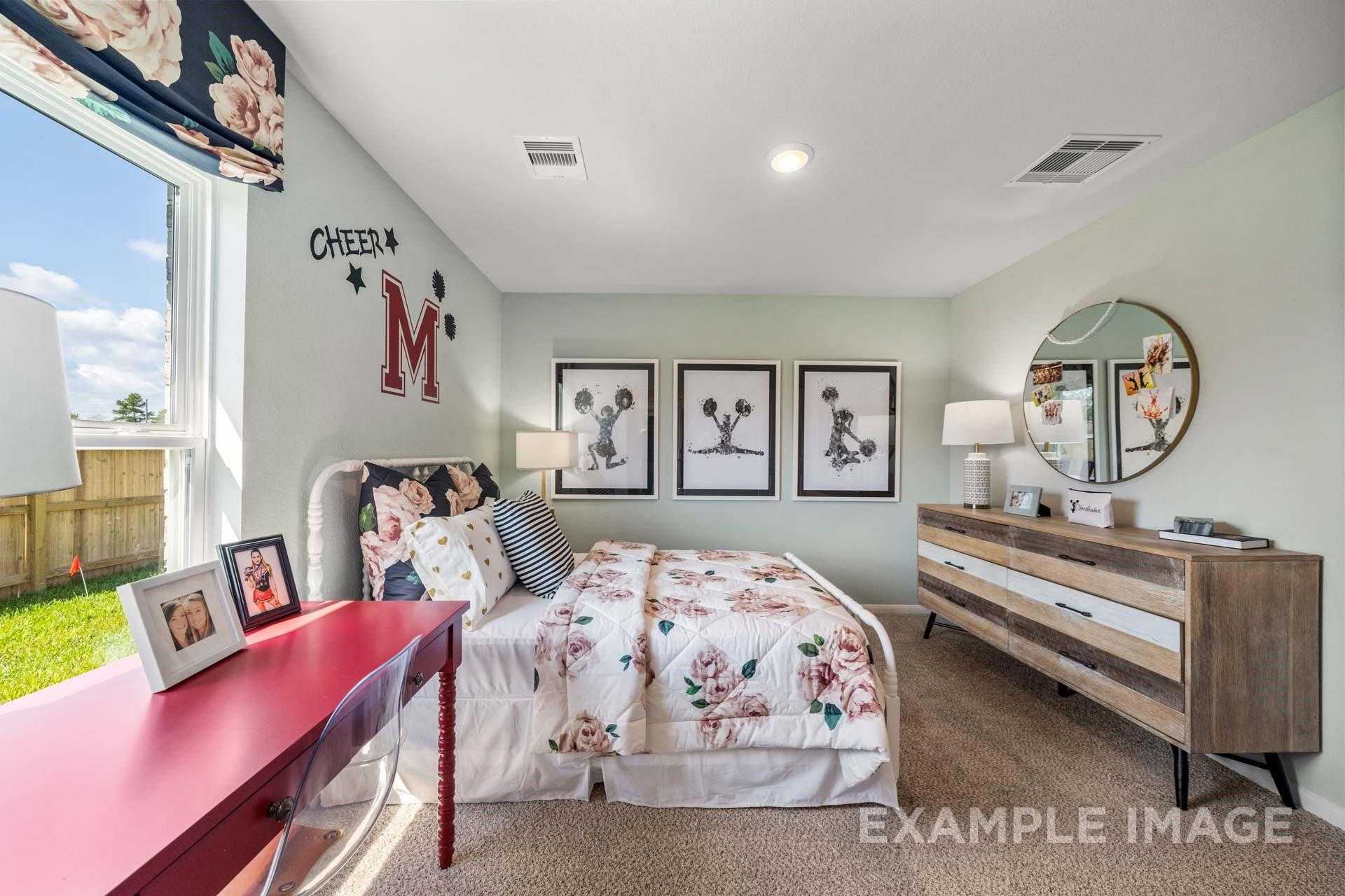 Cheer-themed girl's bedroom with floral bedding, red desk, wooden dresser, and cheerleading posters in 4-bedroom Davidson Homes Acadia A, Texas City