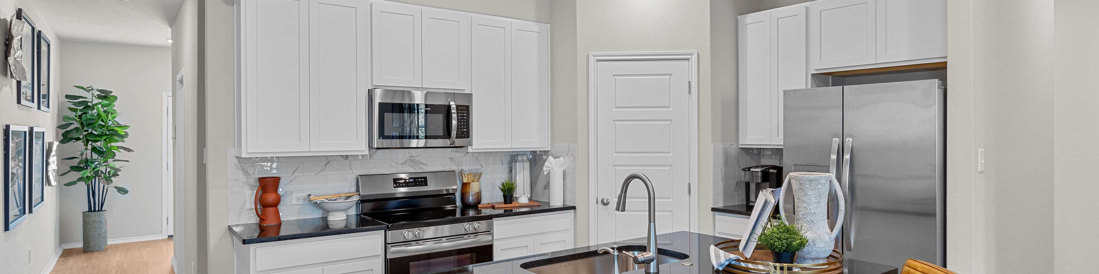 Spacious modern kitchen at Meadows at Oak Creek in San Antonio TX featuring white cabinets, black granite island, stainless steel appliances, and hardwood floors