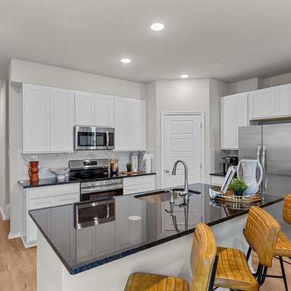 Spacious modern kitchen at Meadows at Oak Creek in San Antonio TX featuring white cabinets, black granite island, stainless steel appliances, and hardwood floors